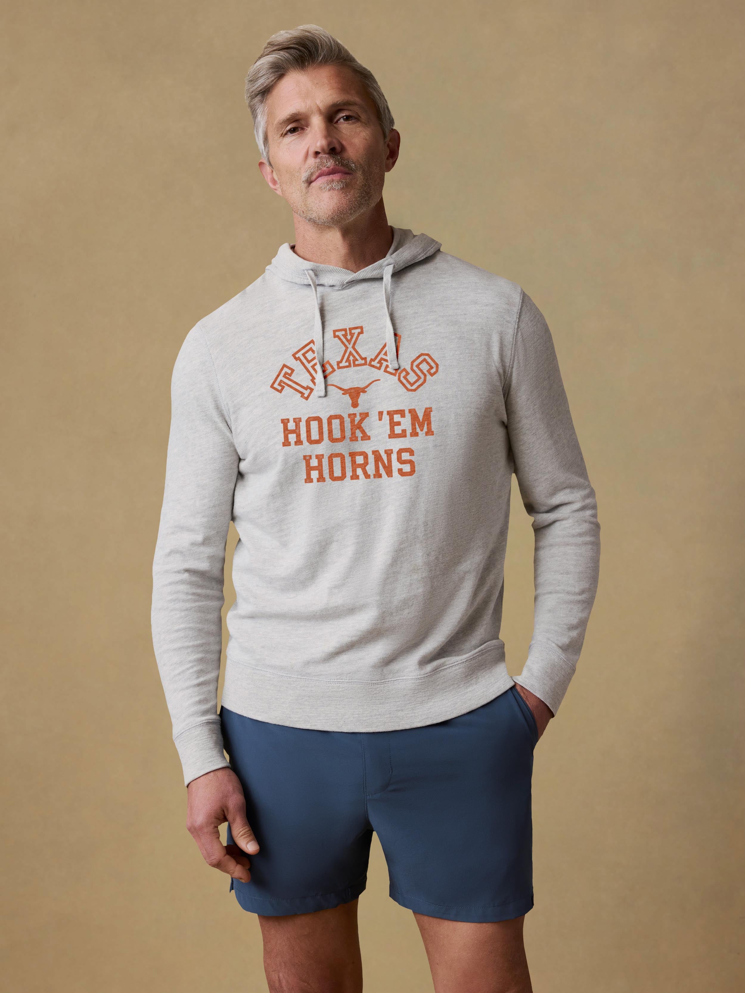 Man is wearing a grey University of Texas hoodie and blue shorts