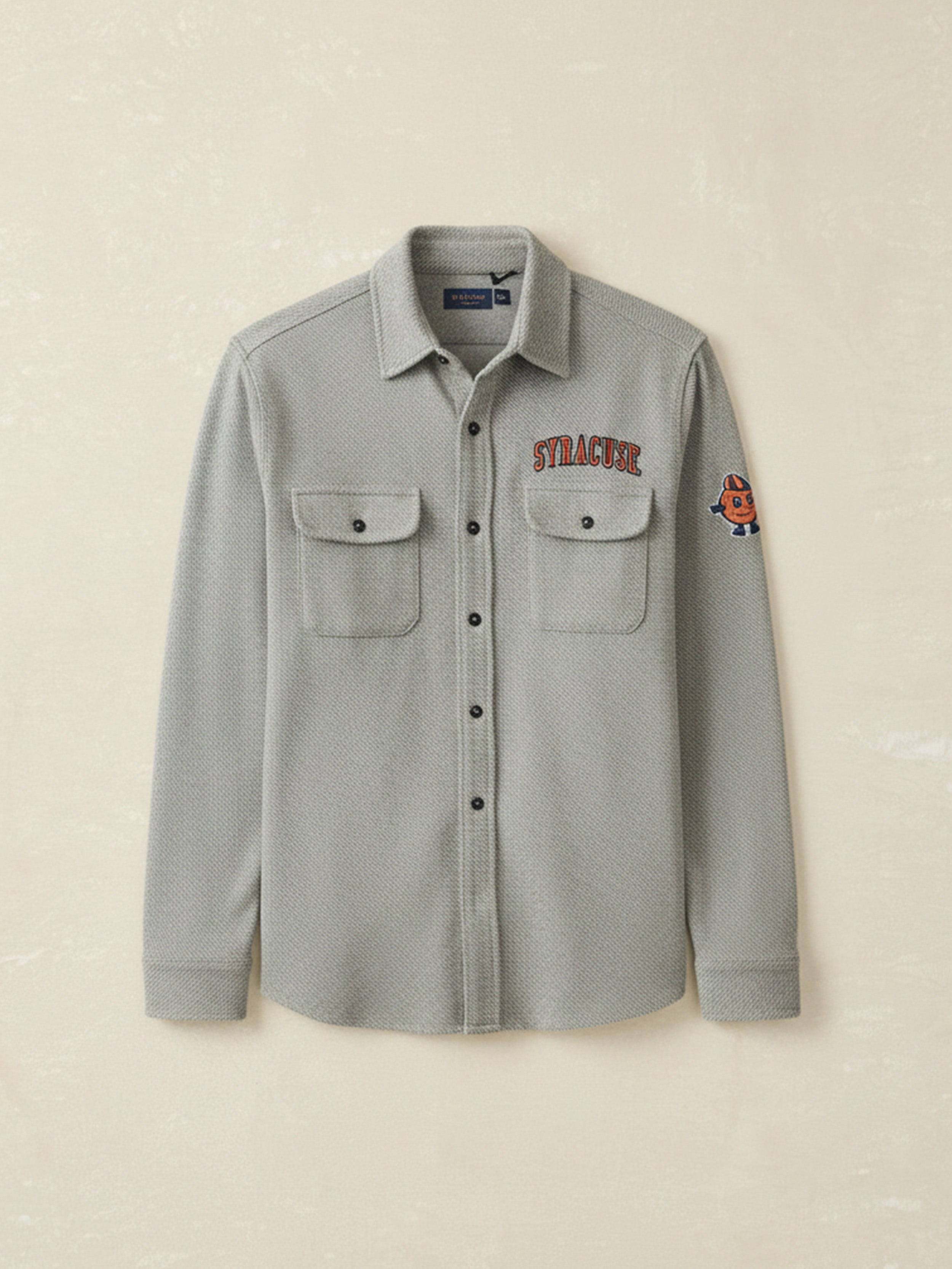 Gray button-up shirt with embroidered Syracuse University graphics against a beige background