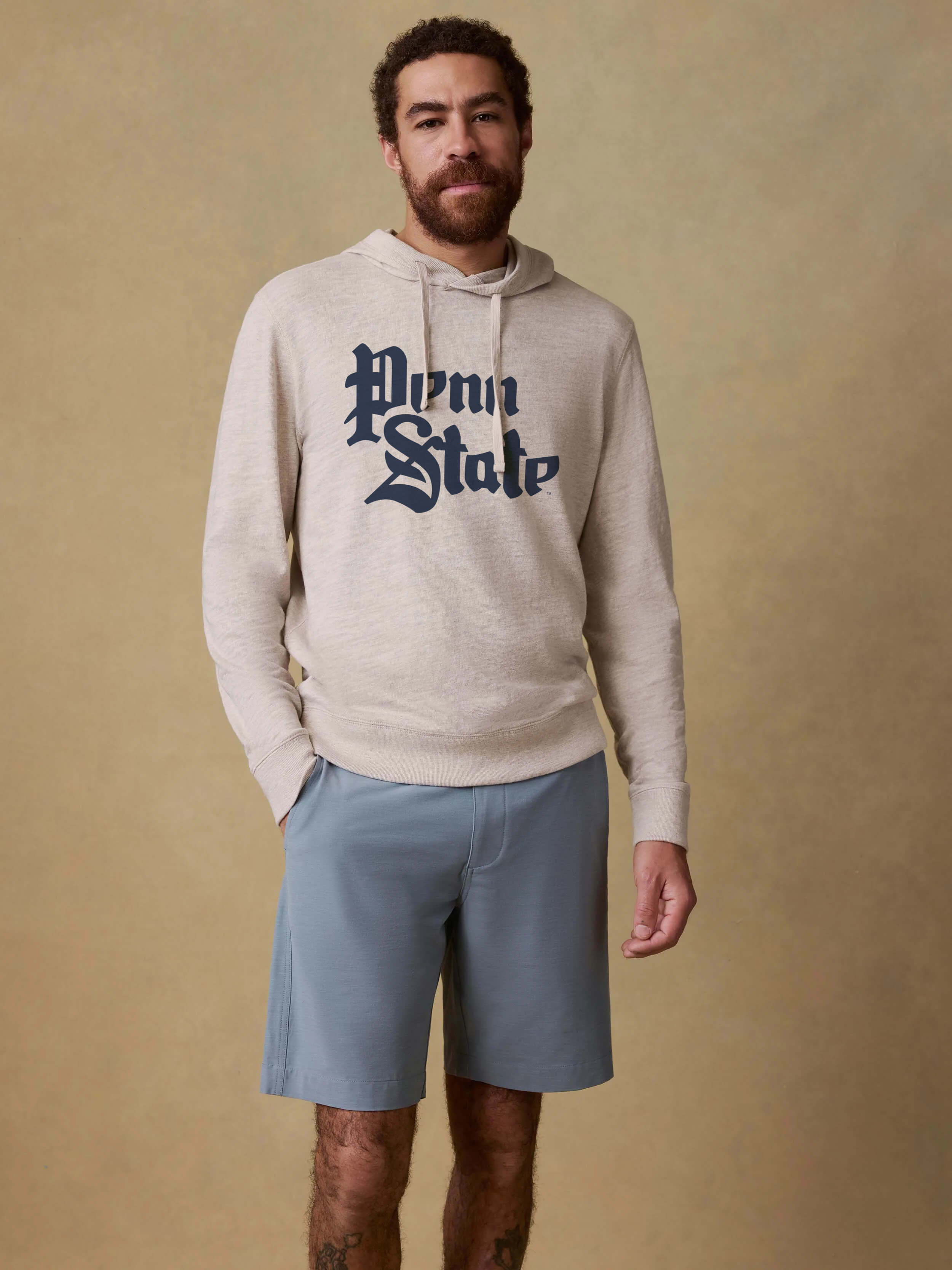 Man wearing a beige hoodie with 'Penn State' text at the center front and light blue shorts against a beige background