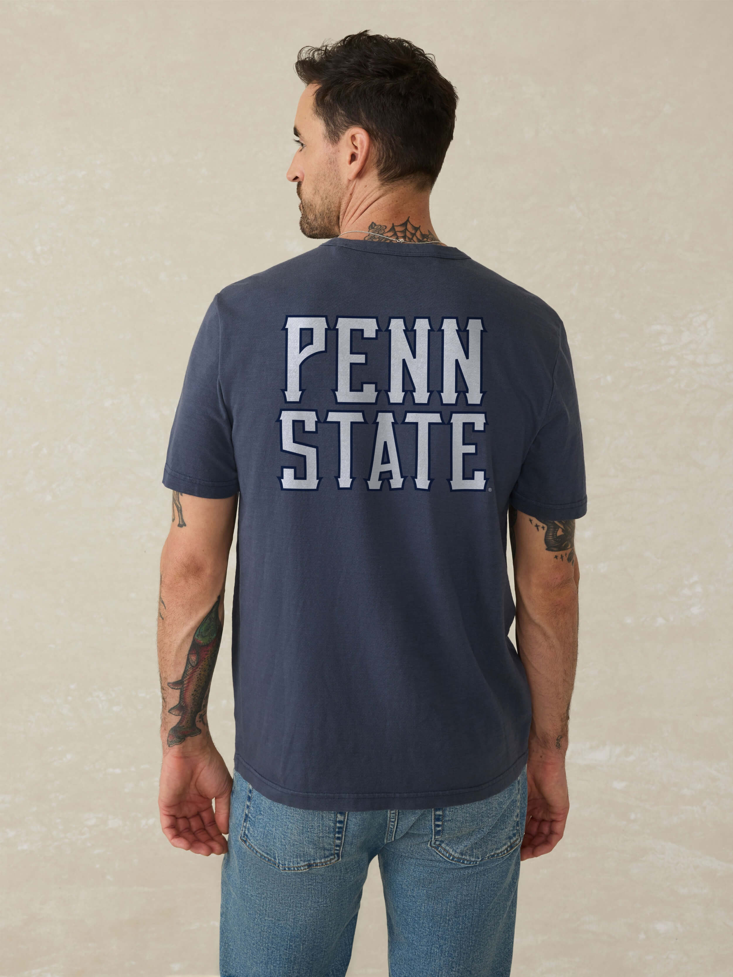 Man wearing a navy blue t-shirt with 'Penn State' printed on the back against a beige background
