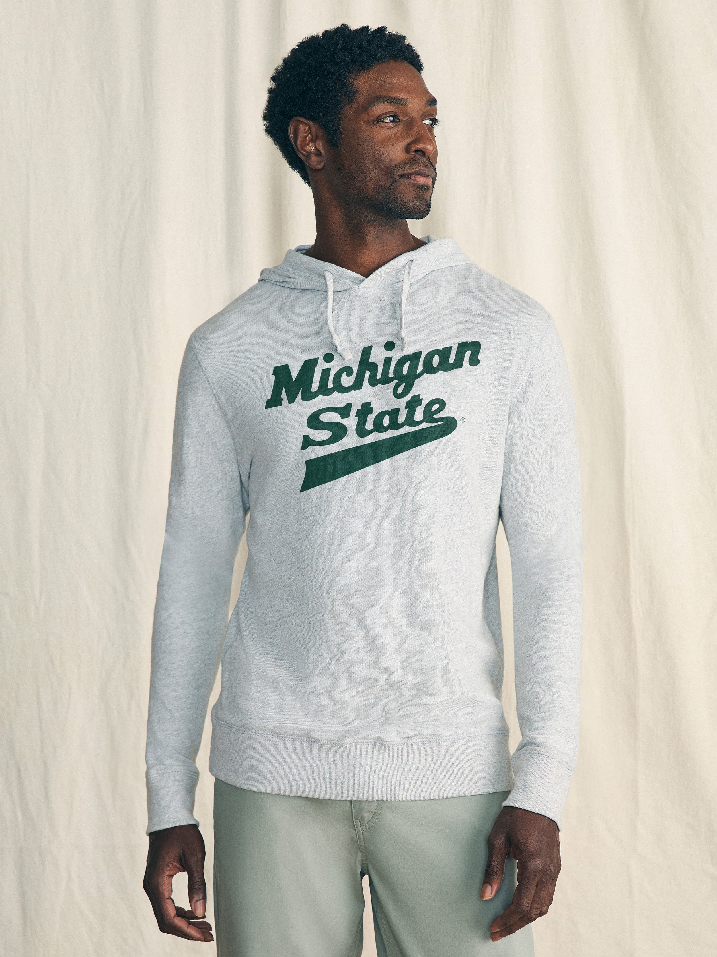 Man wearing a grey hoodie with Michigan State graphic logo at the center front against a beige background