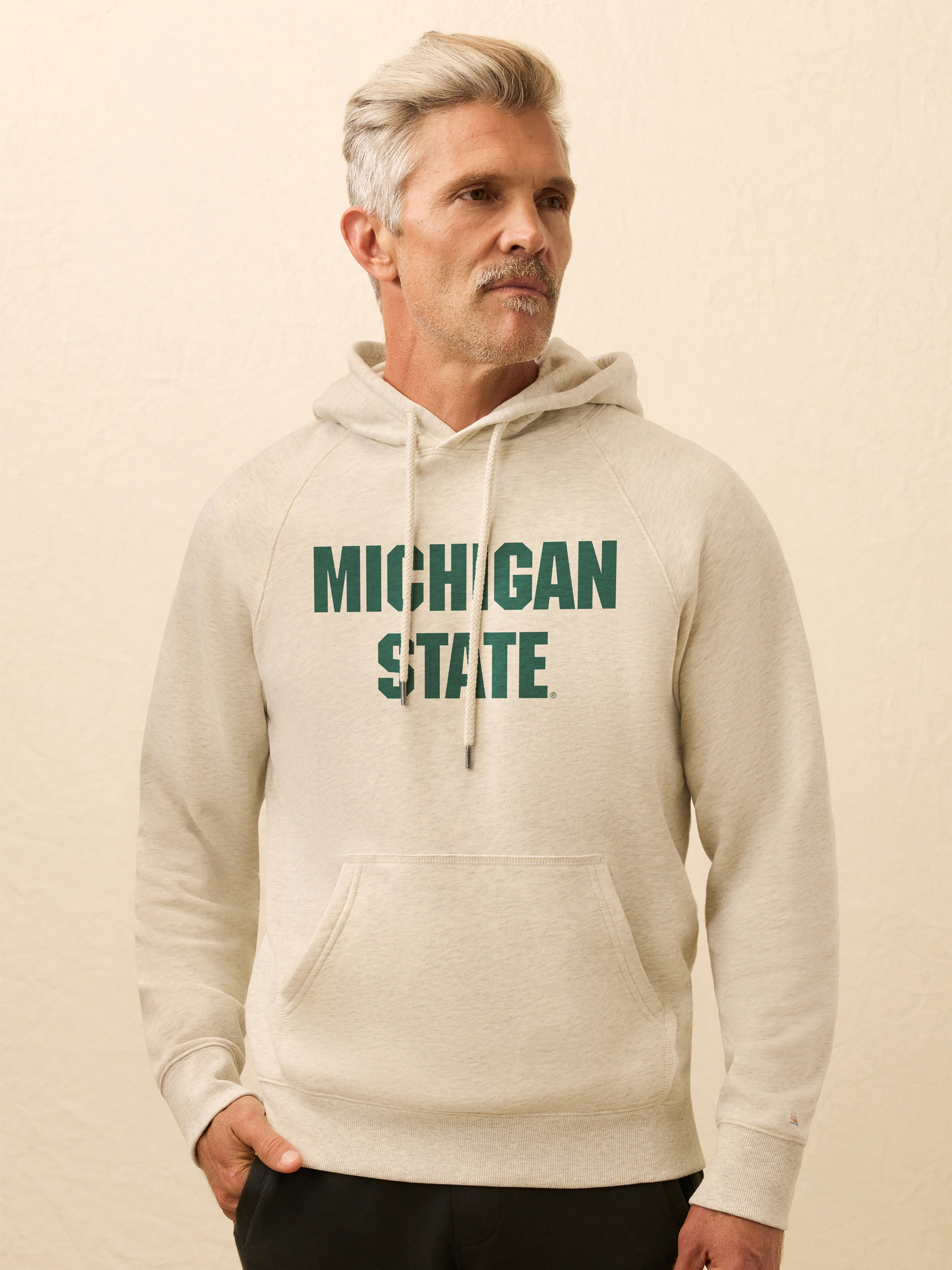 Man wearing a beige hoodie with Michigan State text on a beige background
