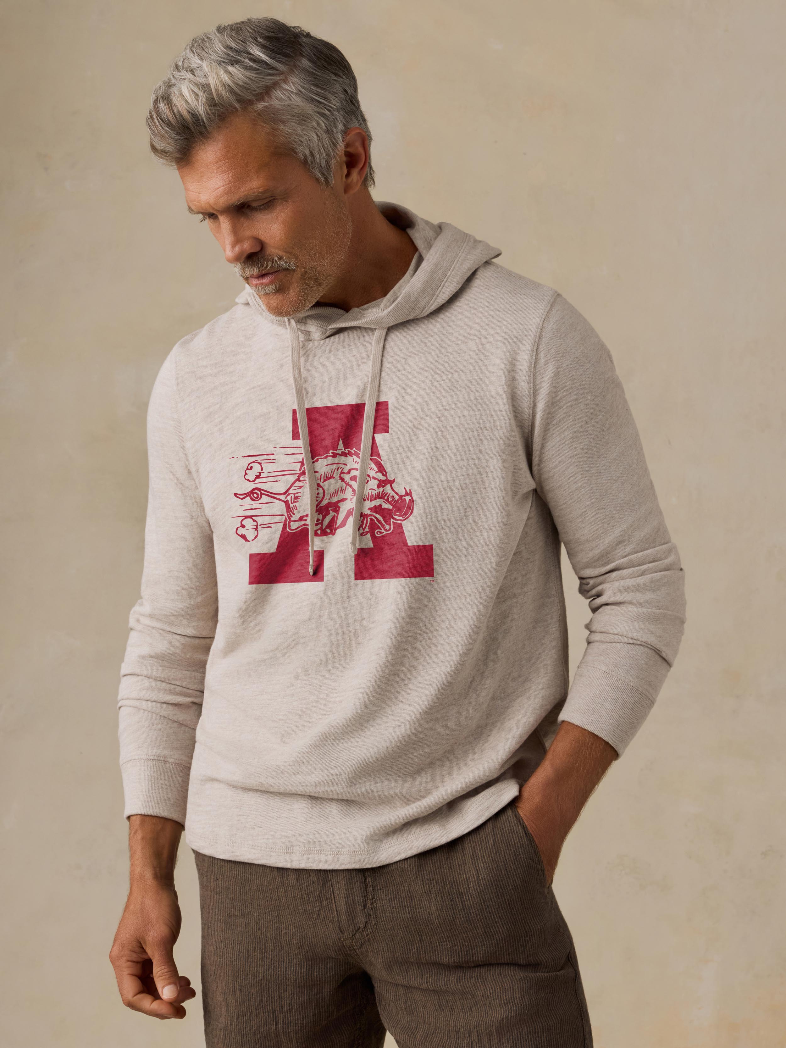 A man is wearing a beige University of Arkansas hoodie and brown shorts
