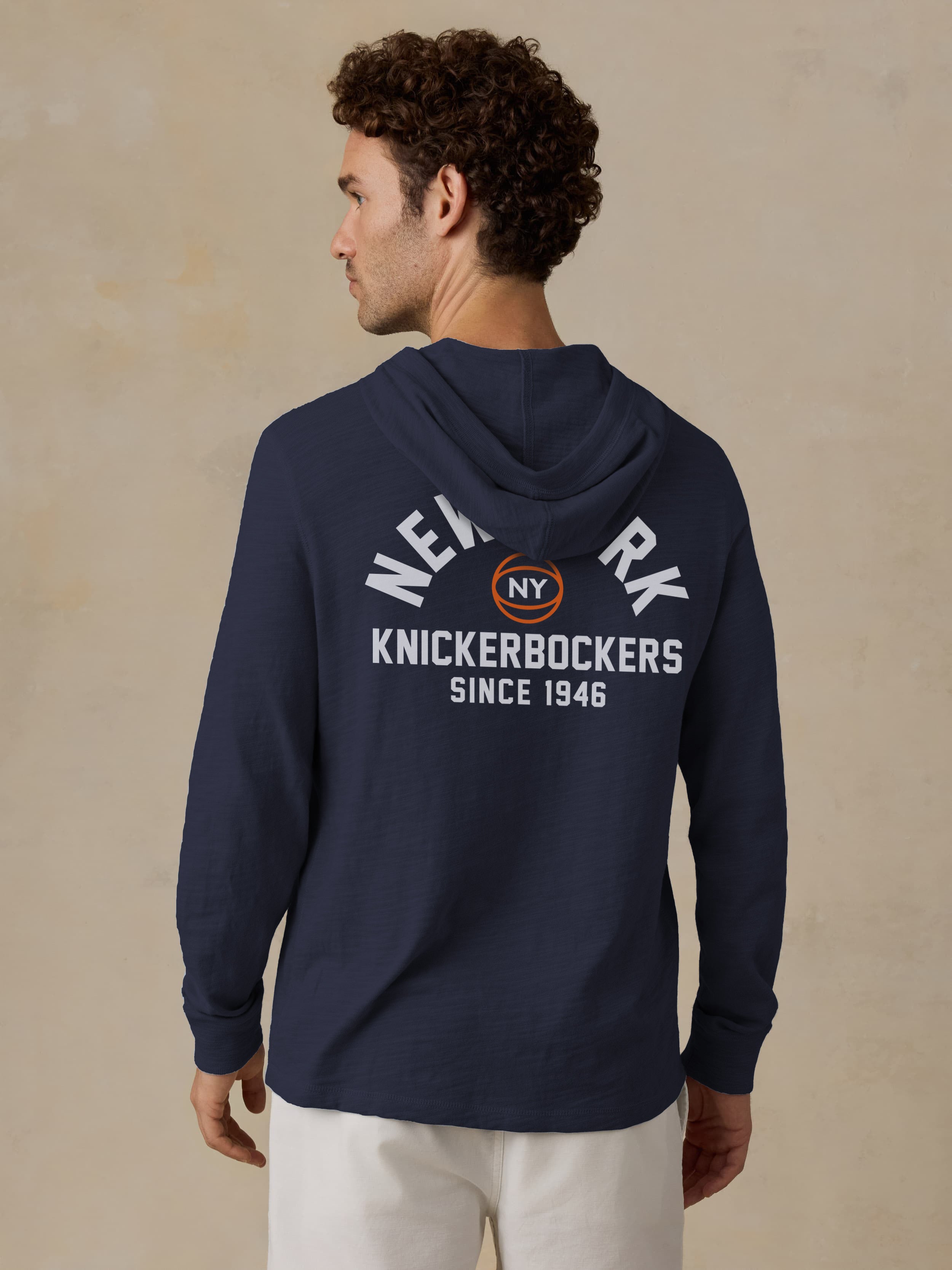 Man wearing a navy blue NY Knicks graphic on the back against a beige background