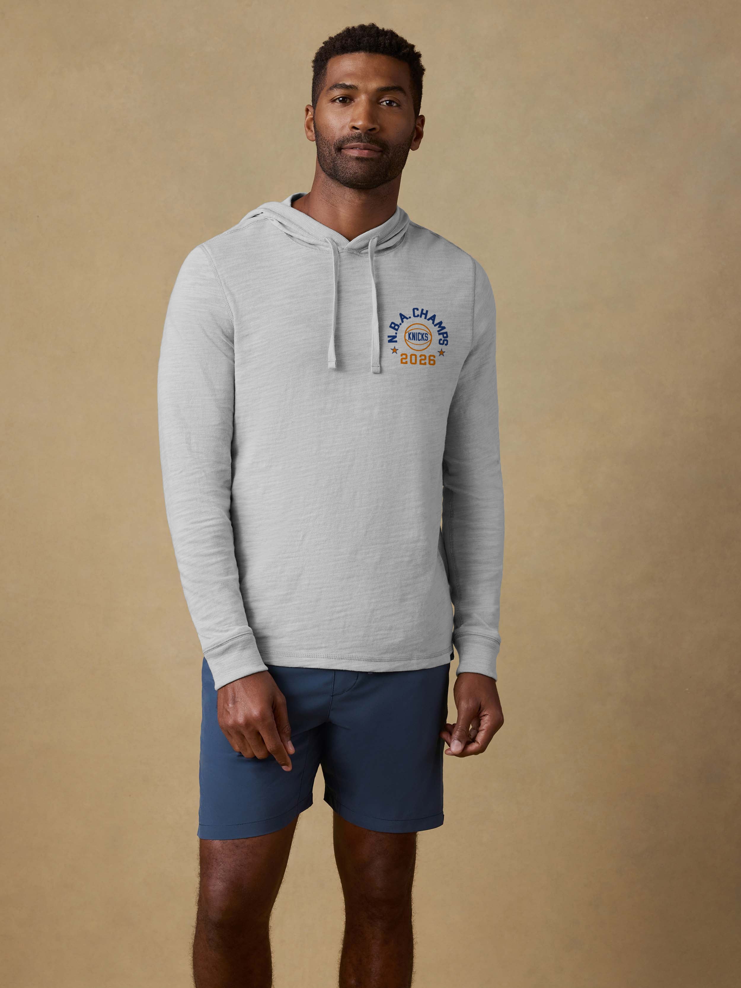 Man wearing a grey hoodie with a NY Knicks NBA Champs graphic on the left chest against a beige background