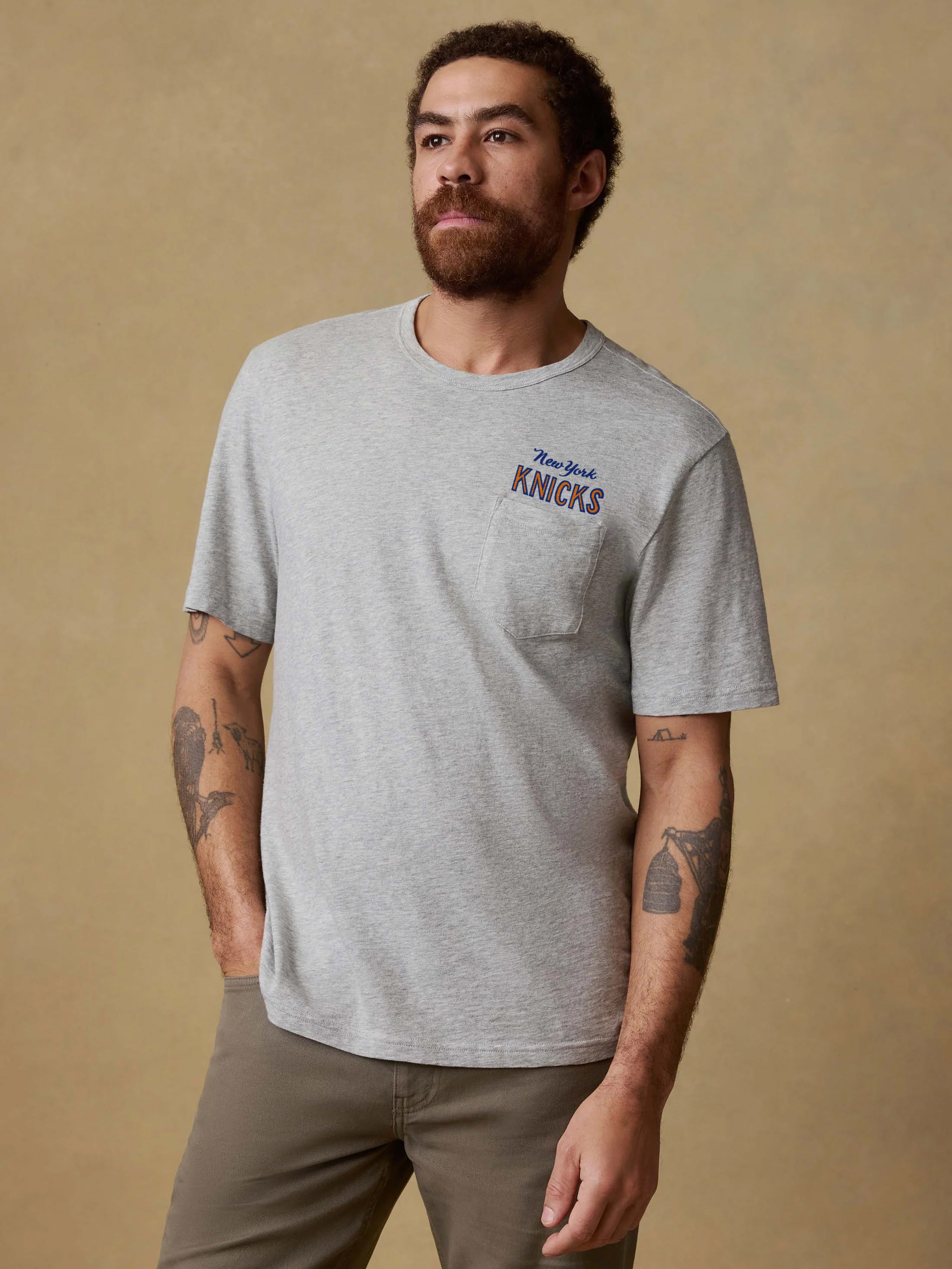 Man wearing a gray t-shirt with 'New York Knicks' graphic on the left chest against a beige background