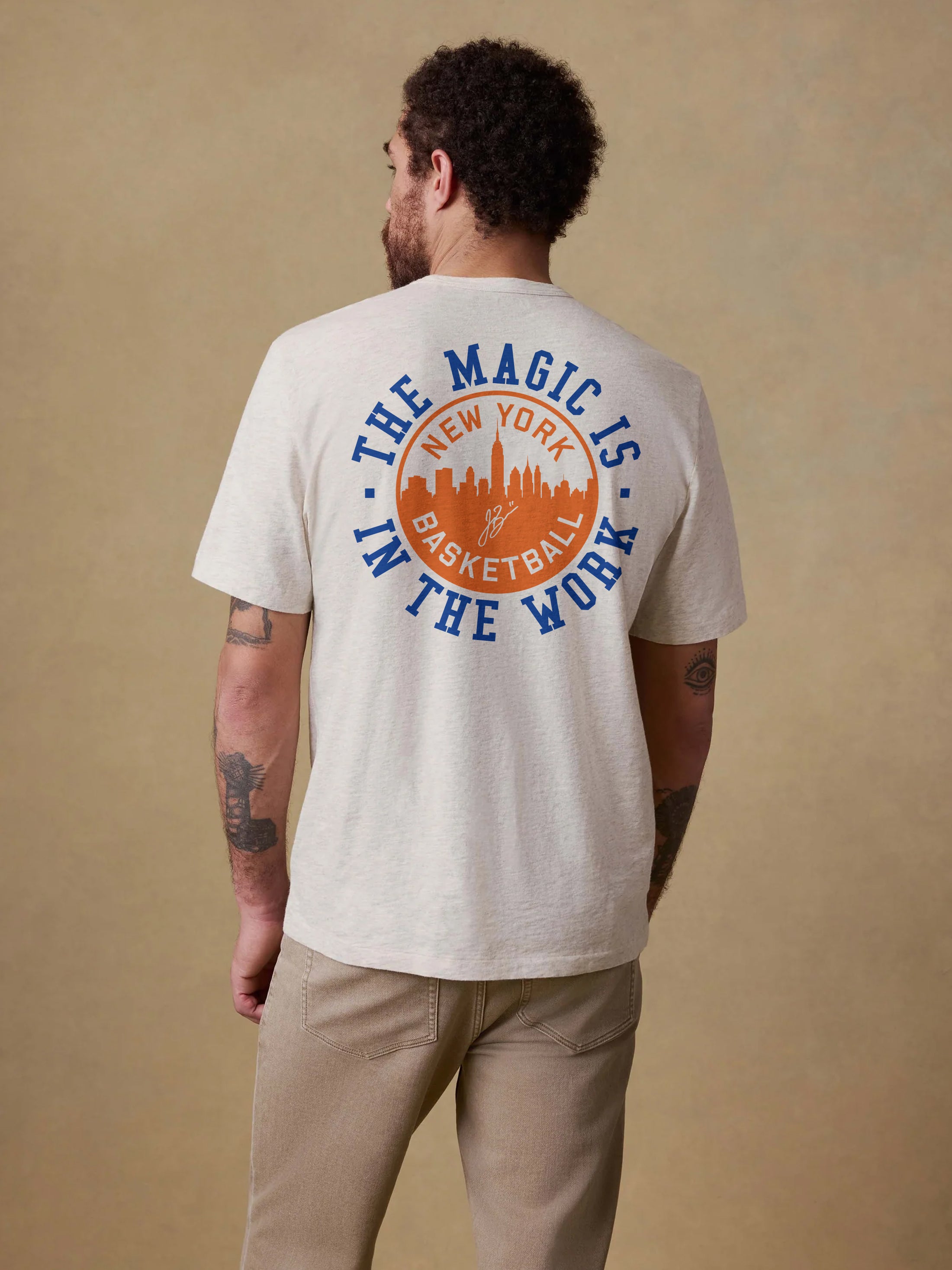 Man wearing a t-shirt with 'The Magic is in the Work' New York Basketball design on the back against a beige background