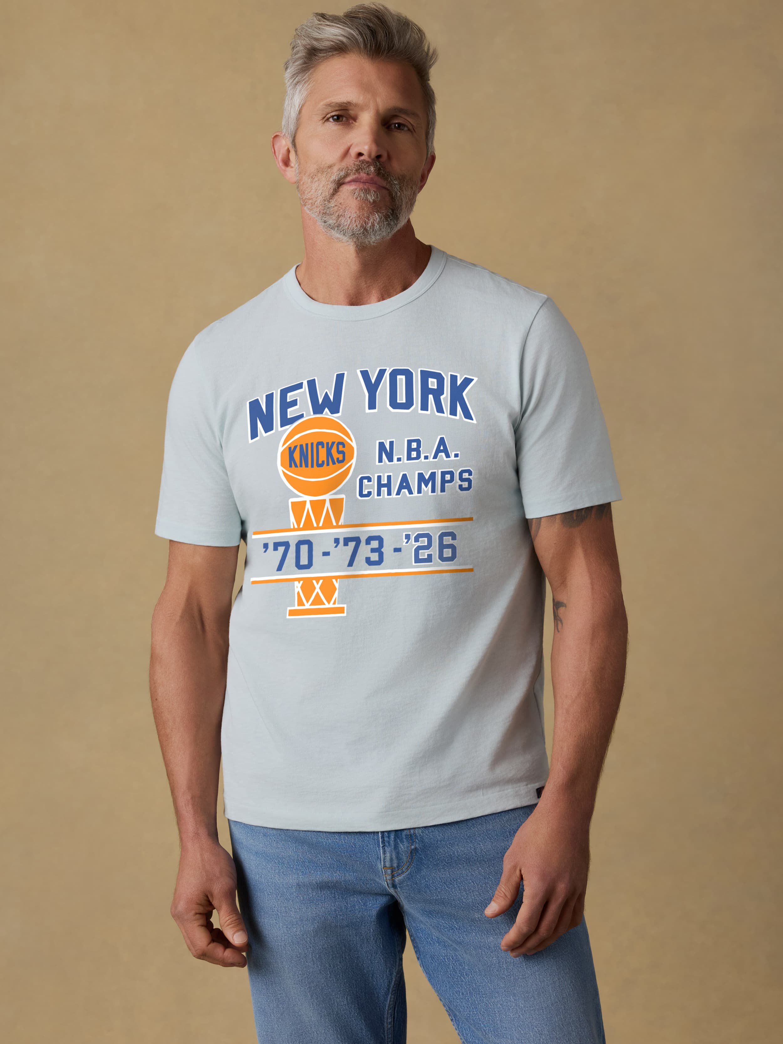 Man wearing a light blue t-shirt with NY Knicks graphic on the center front against a beige background