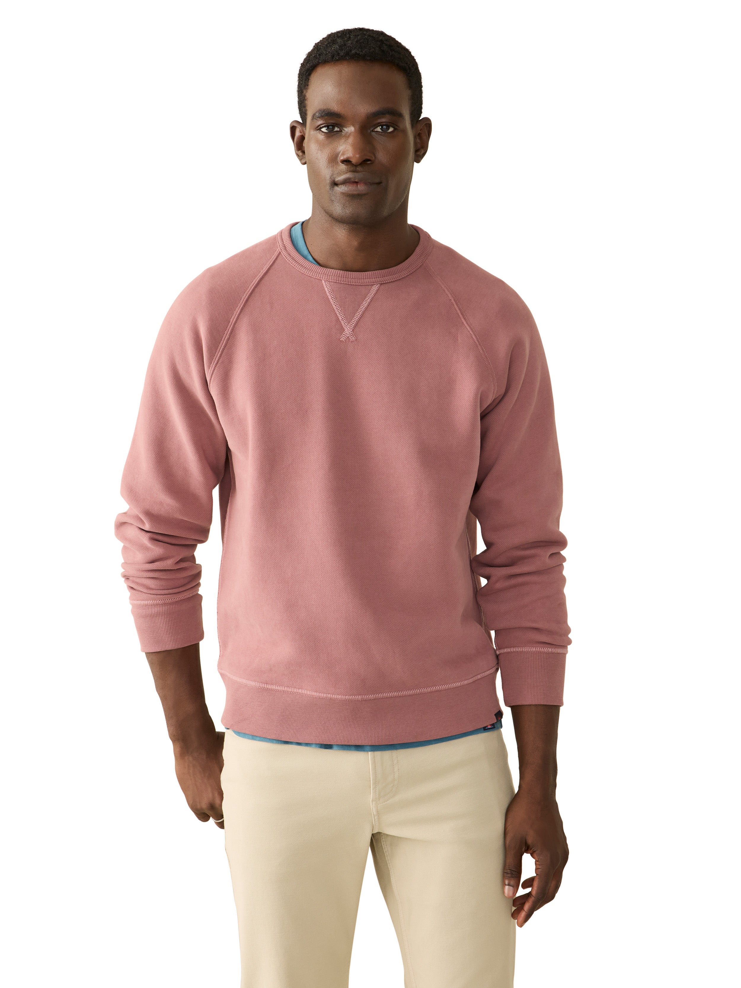 A man wearing a pink crewneck and beige pants