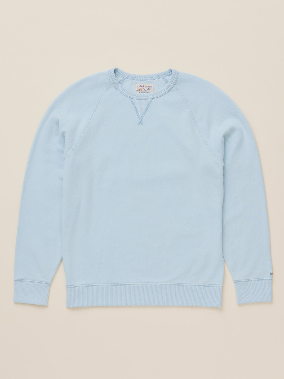 A light blue crewneck sweatshirt with raglan sleeves, laid flat against a solid beige background., image 6 of 7