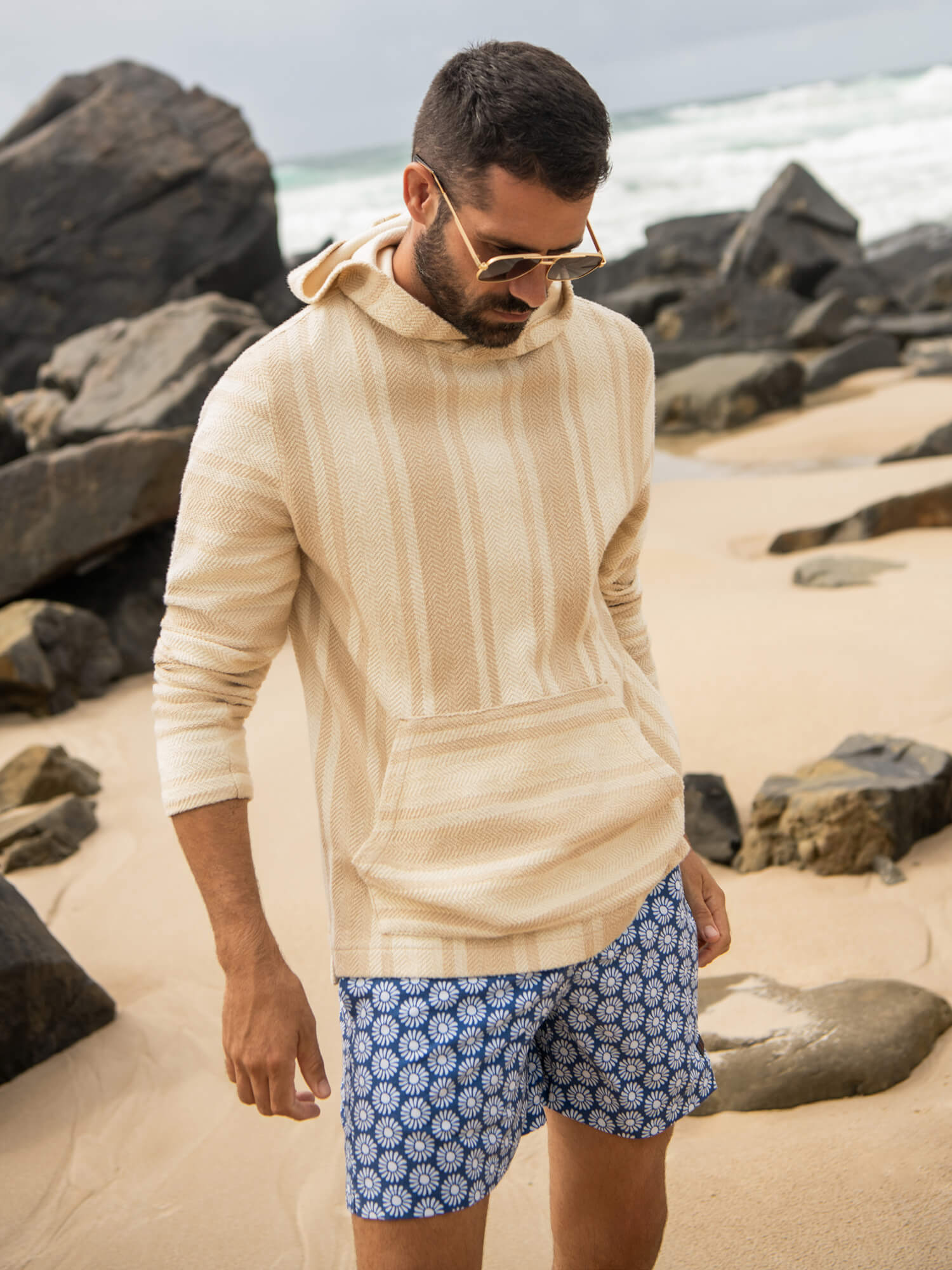 Man wearing a striped hoodie and printed swim trunks at the beach