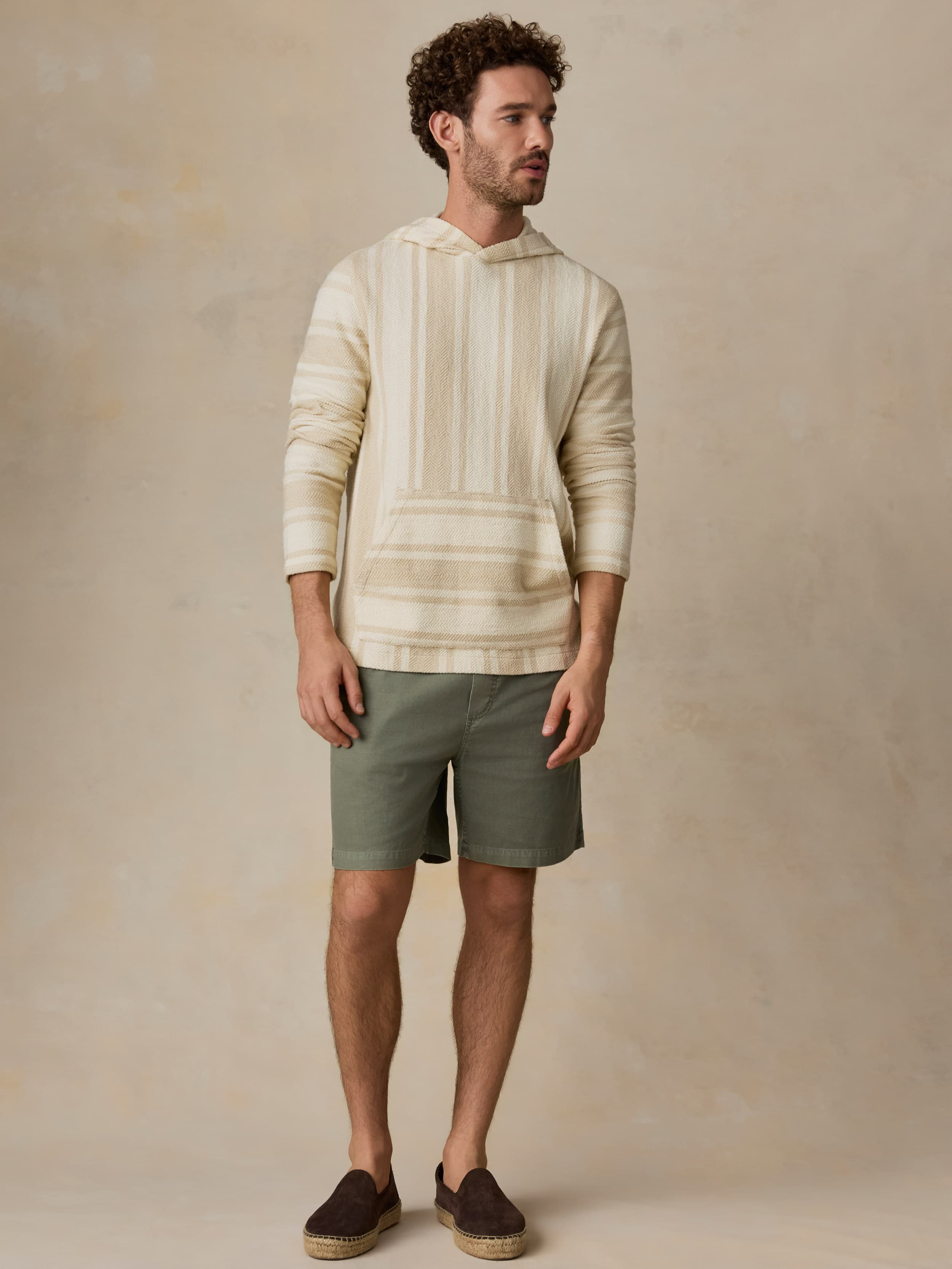 Man wearing a beige striped hoodie and green shorts against a beige background