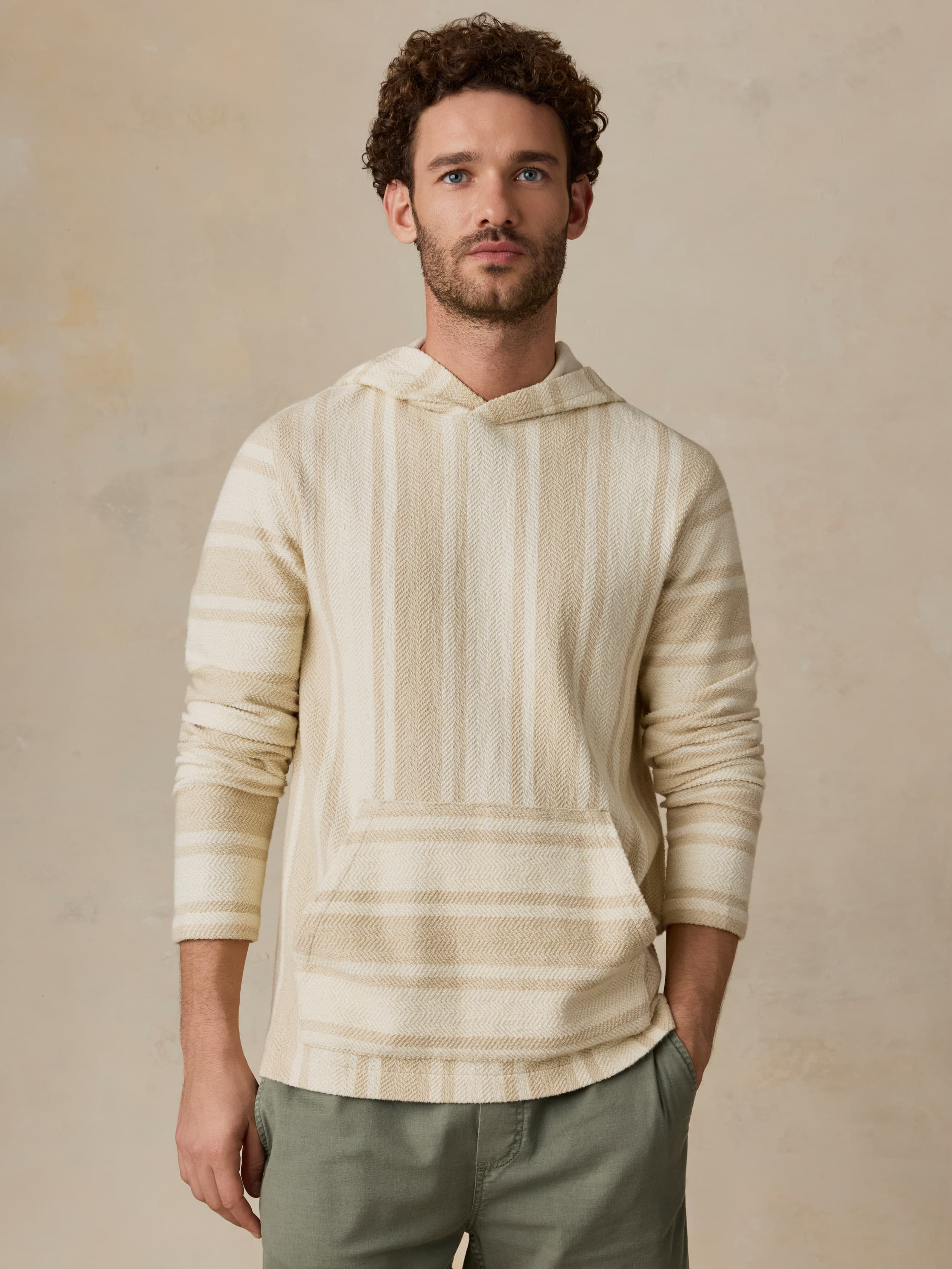 Man wearing a cream-colored striped hoodie against a beige background