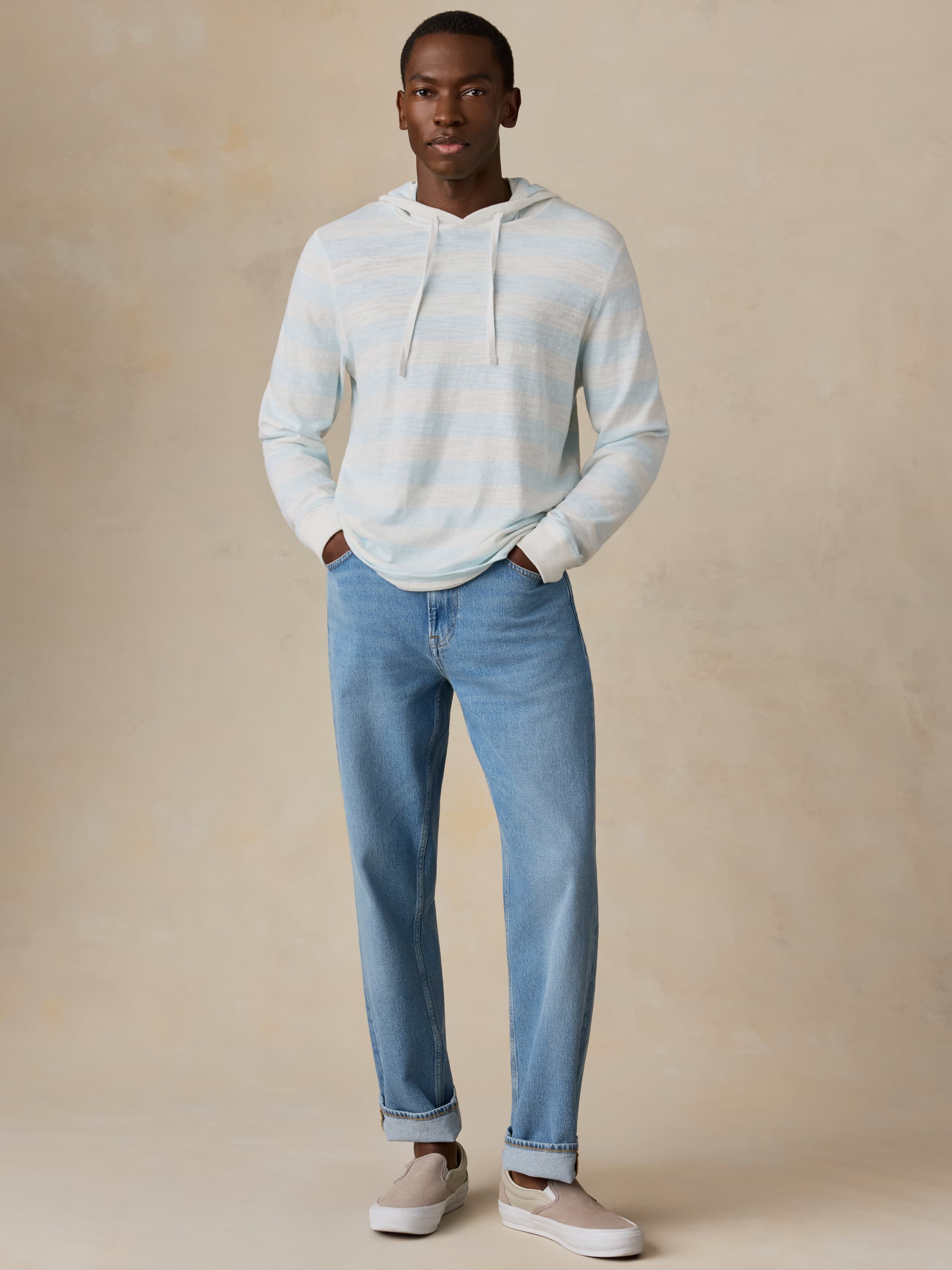 Man wearing a light blue striped hoodie and jeans against a beige background