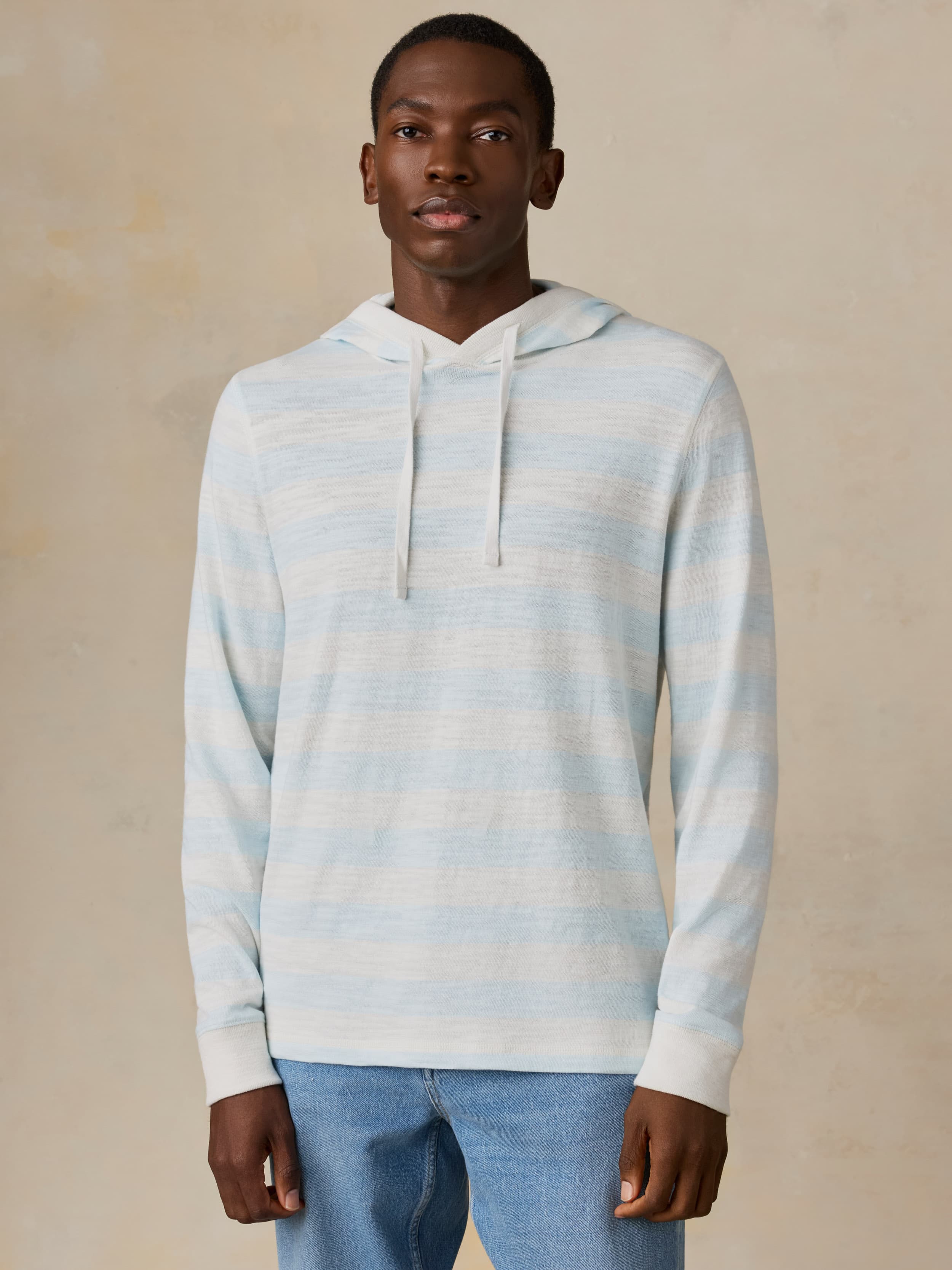 Man wearing a light blue and white striped hoodie against a beige background