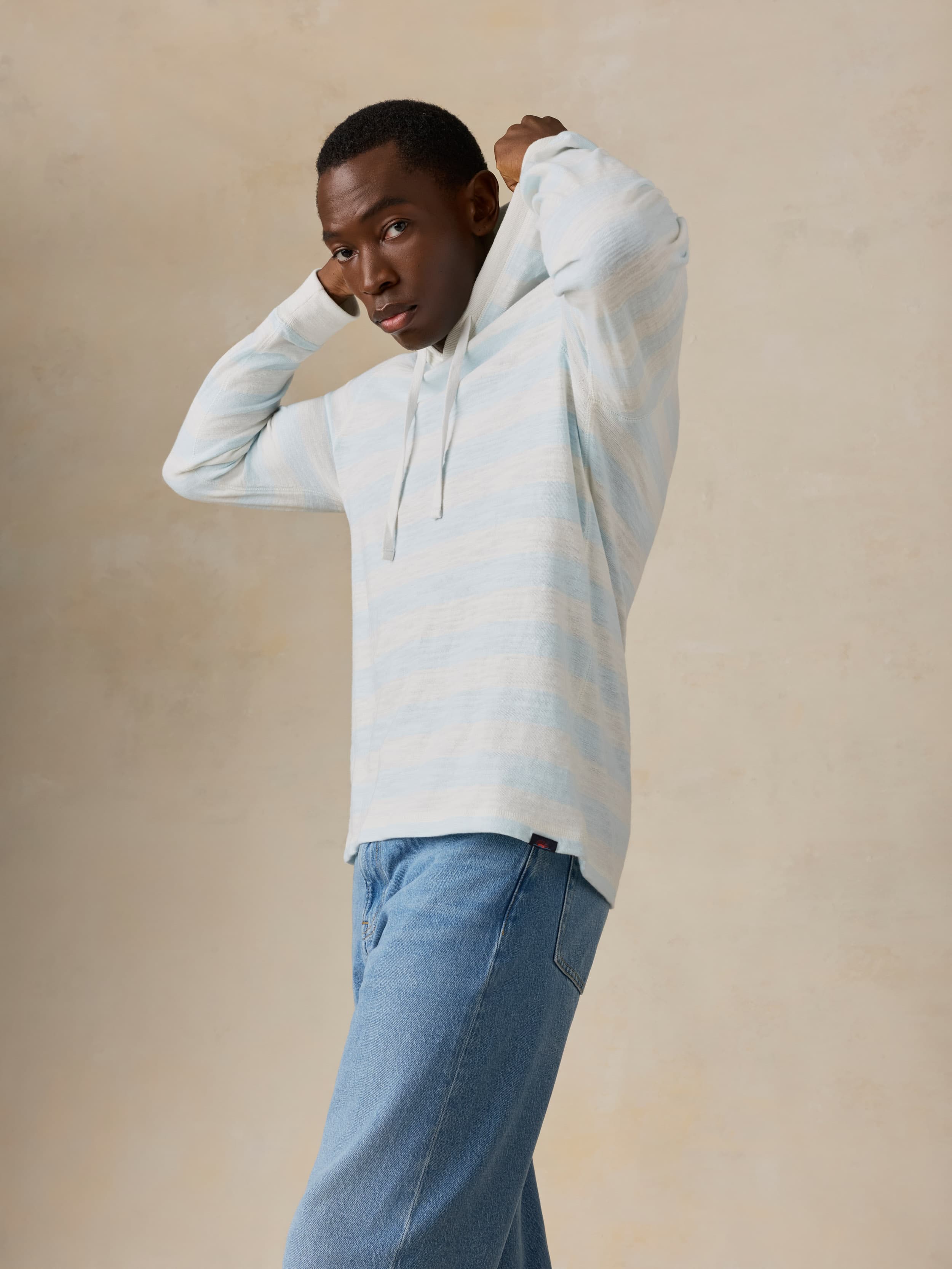 Man wearing a light blue striped hoodie and jeans against a beige background