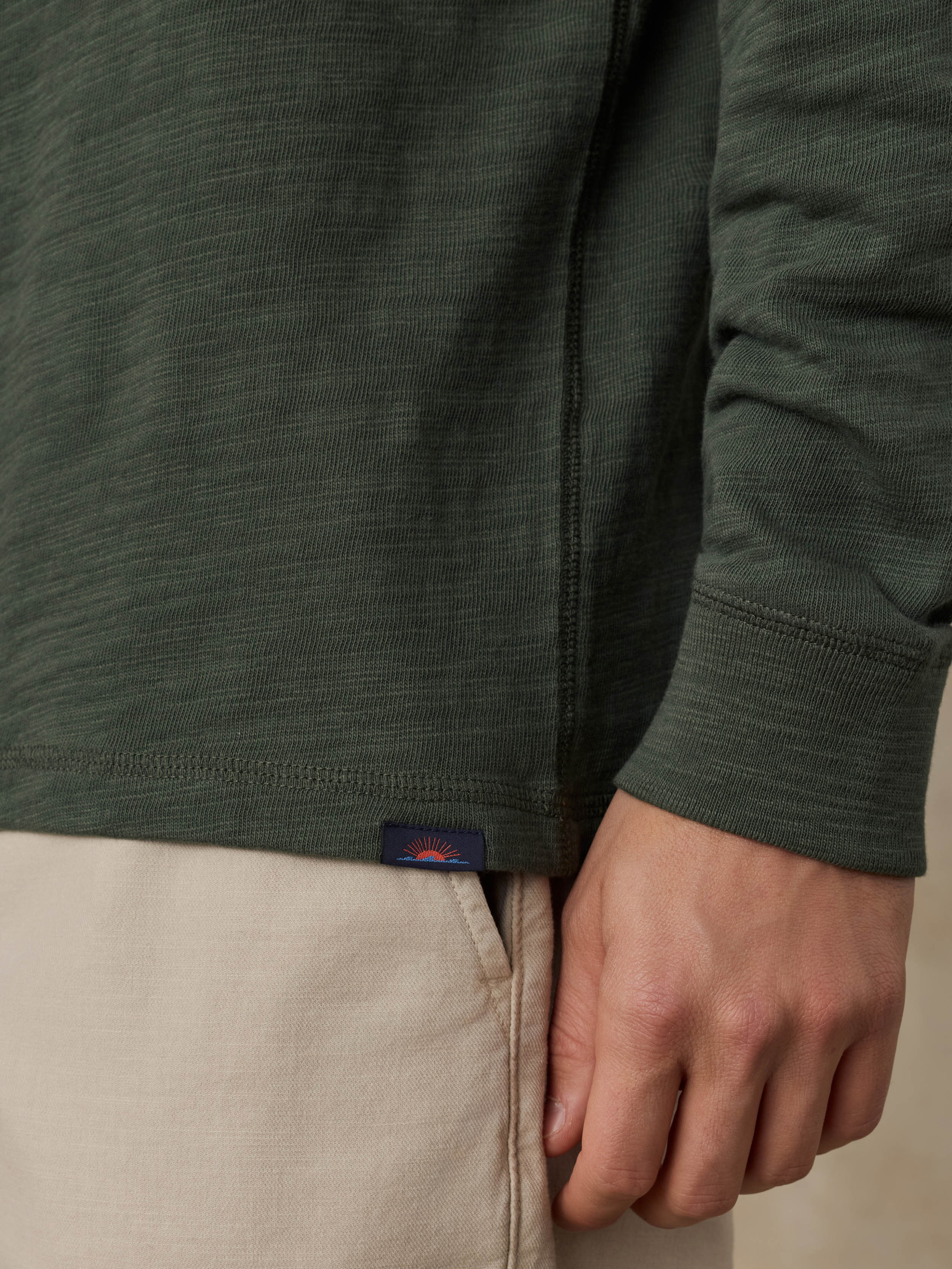 Close-up of a man wearing a dark olive green hoodie and beige shorts against a beige background