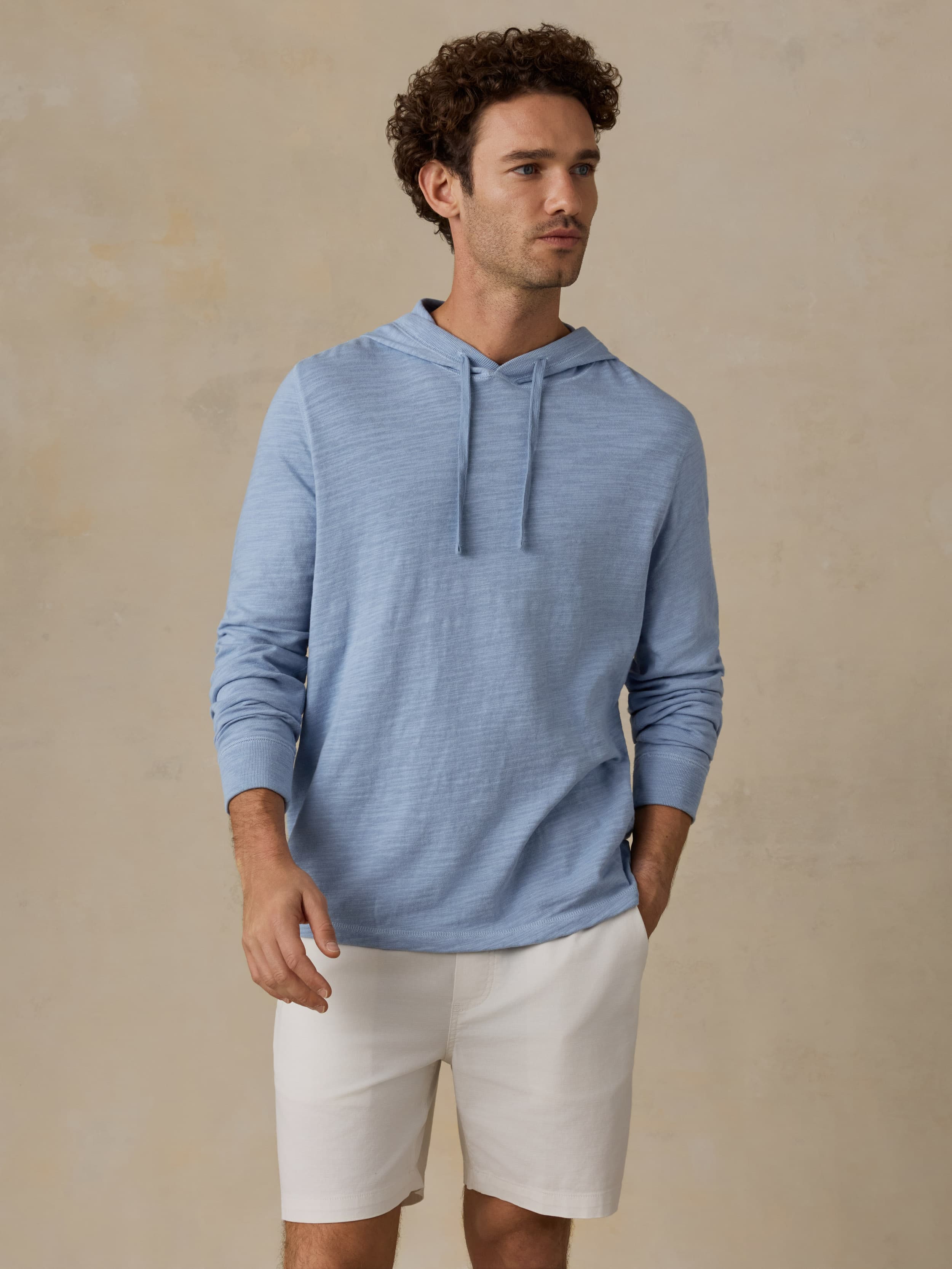 Man wearing a blue hoodie and beige shorts against a beige background