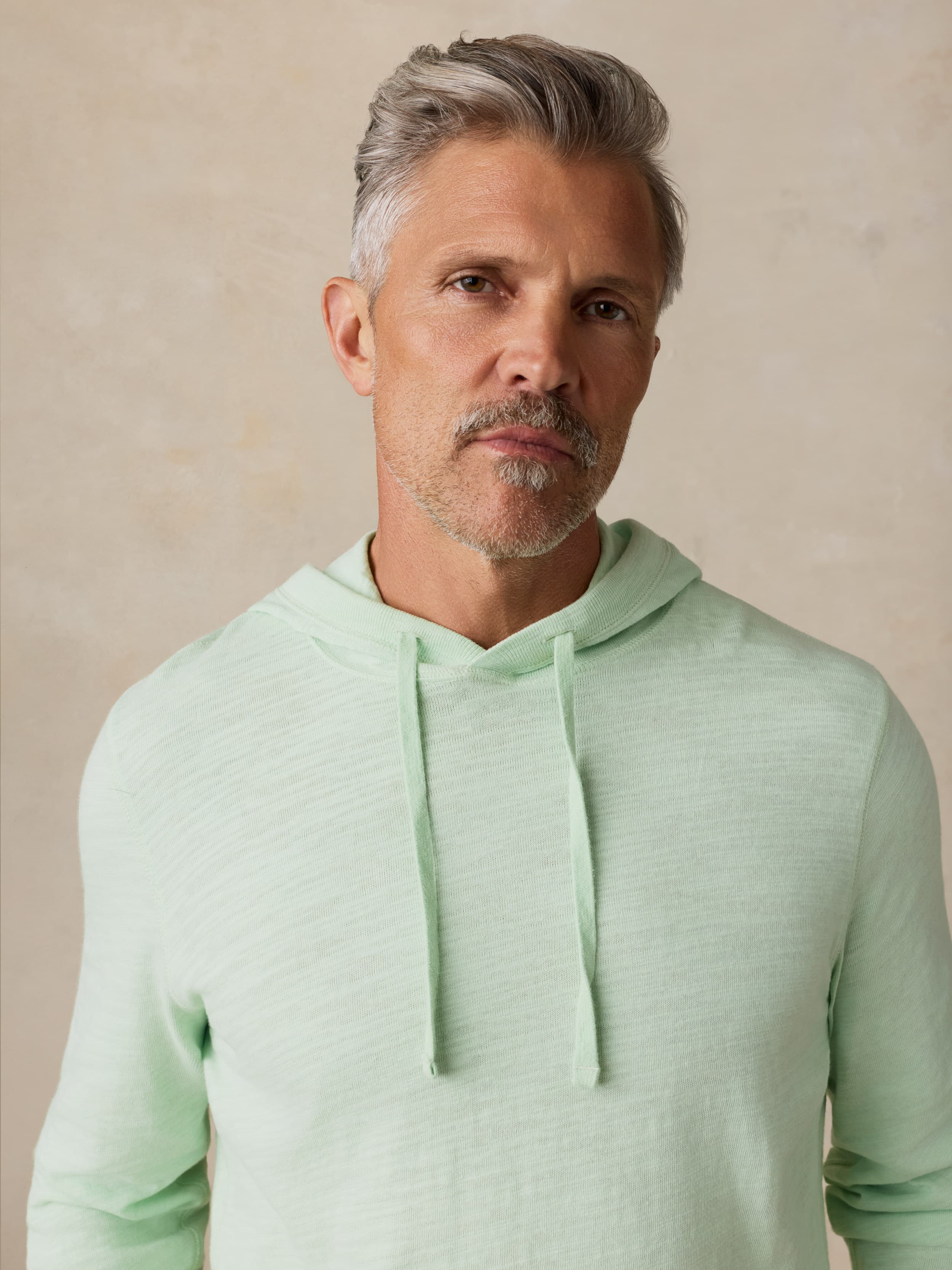 Man wearing a light green hoodie against a beige background