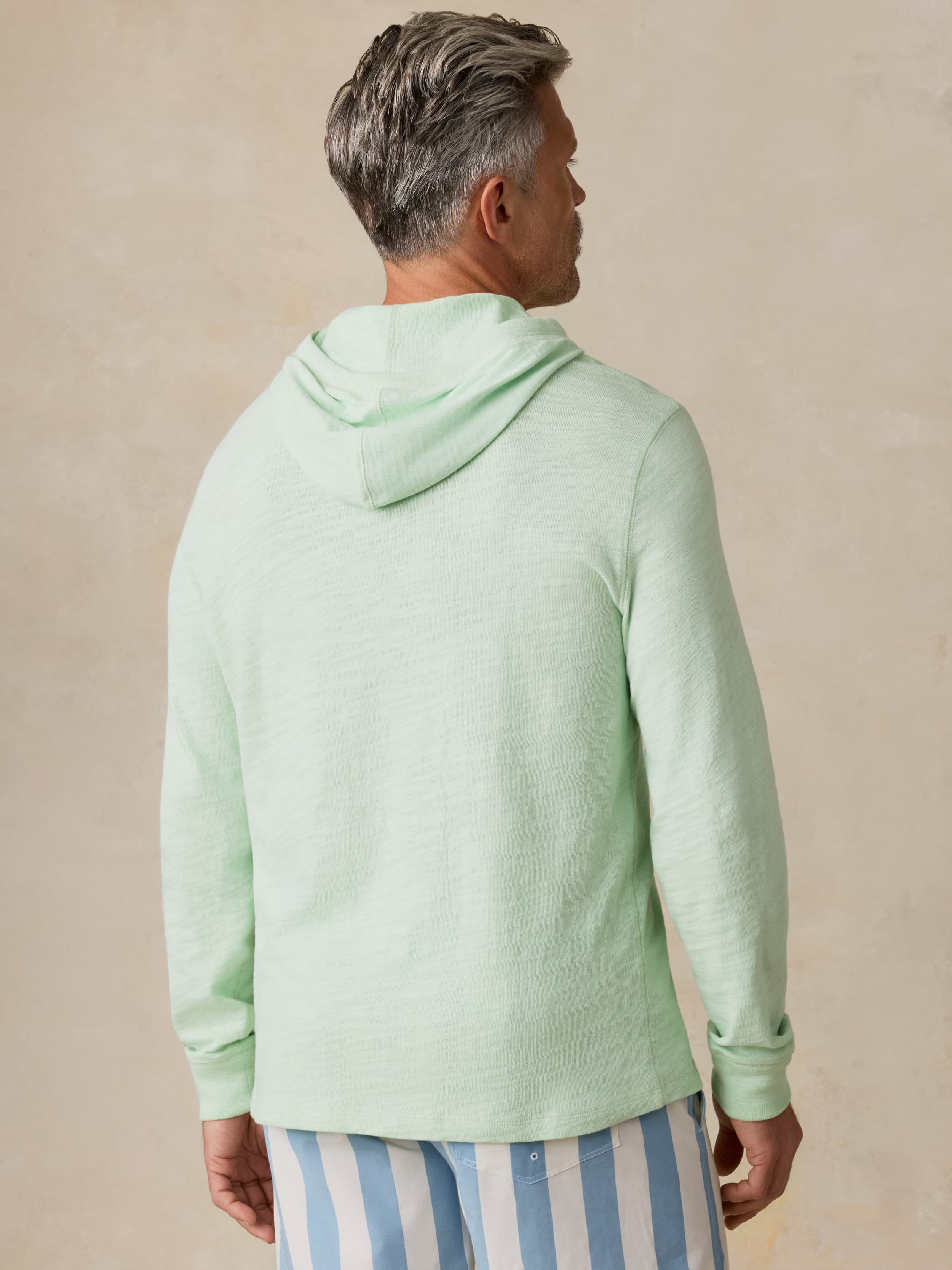 Man wearing a light green hoodie and striped pants against a beige background