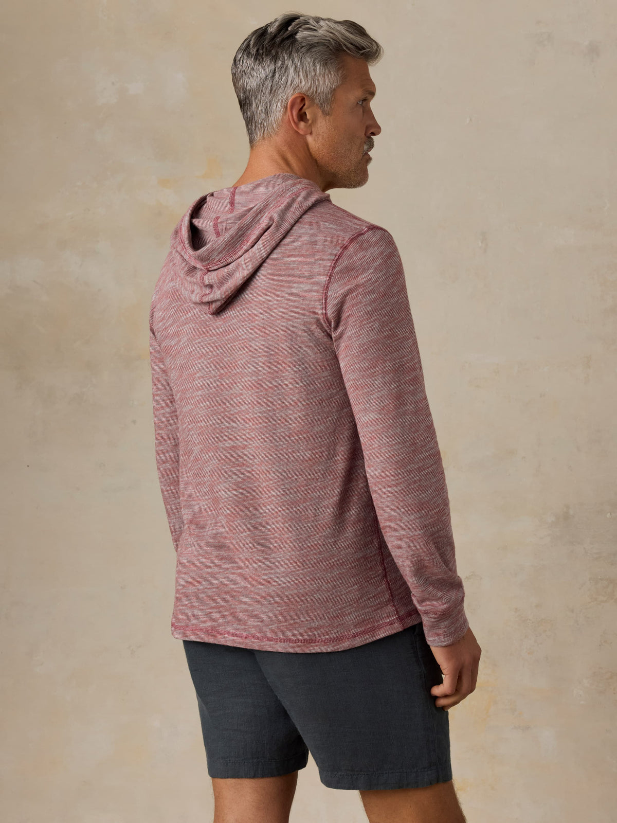 Man wearing a red heathered hoodie and black shorts against a beige background, image 4 of 5