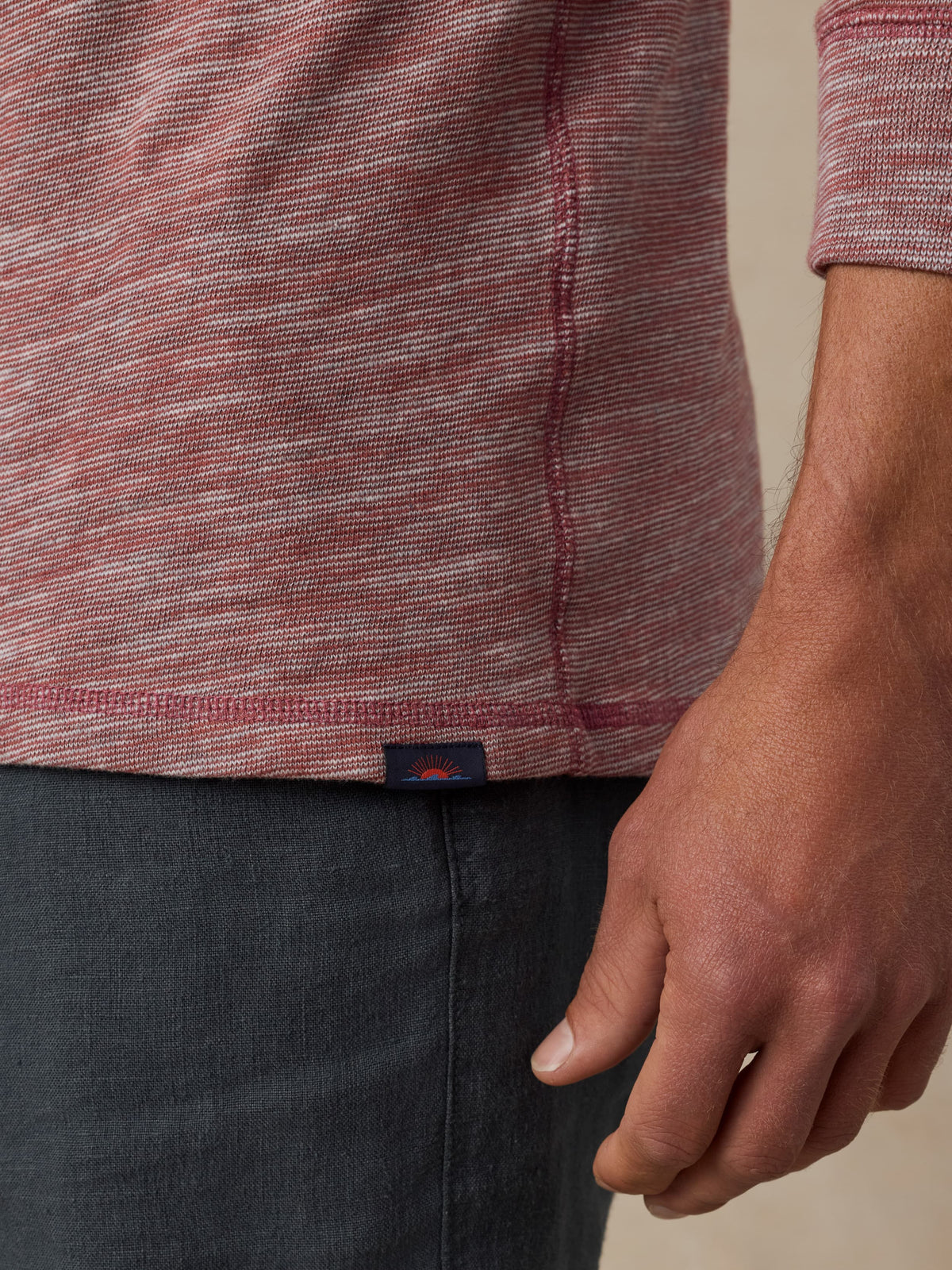Close up of a man wearing a red heathered hoodie with a visible Faherty brand label and black shorts against a beige background, image 3 of 5