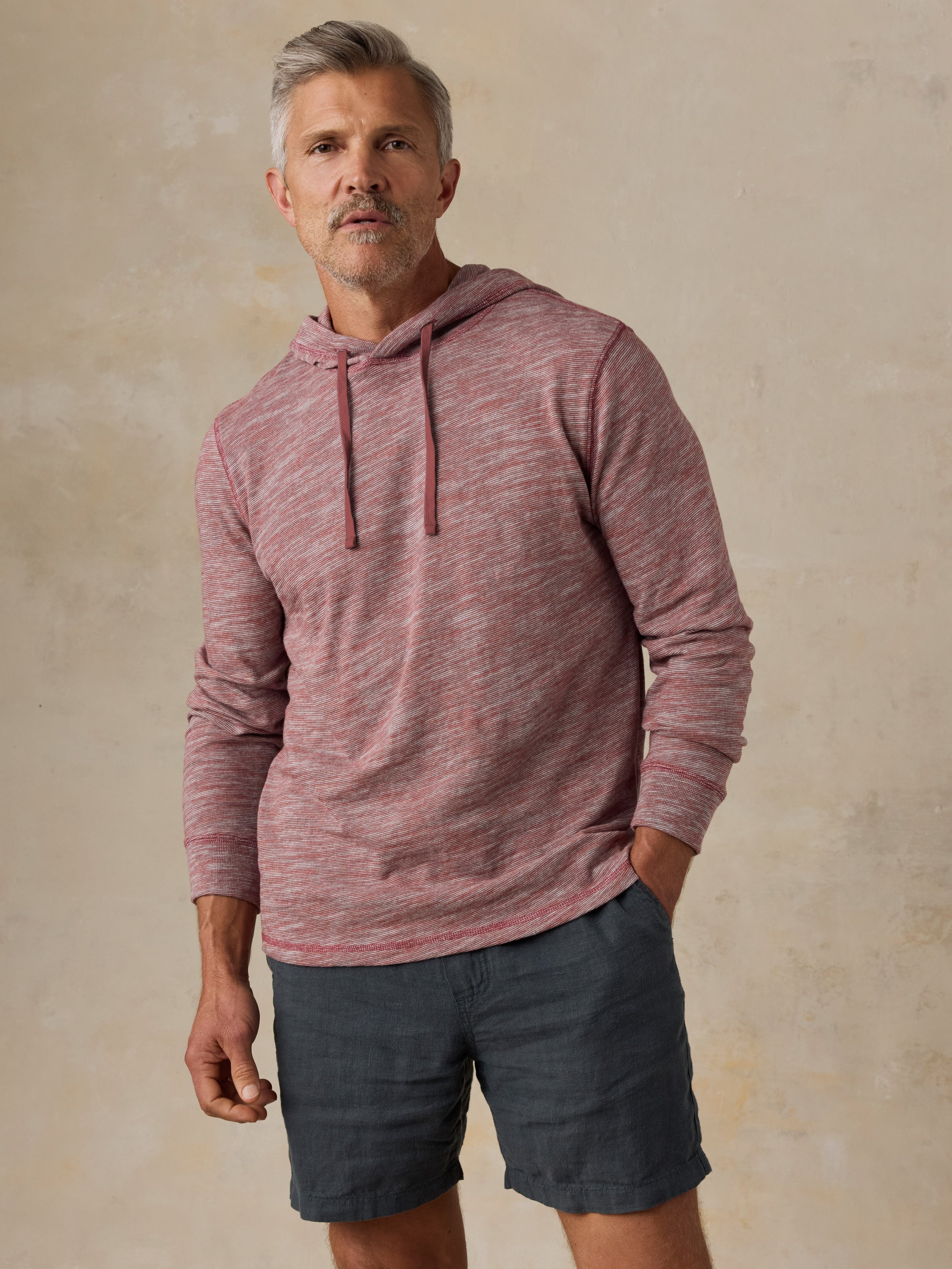 Man wearing a red heathered hoodie and black shorts against a beige background