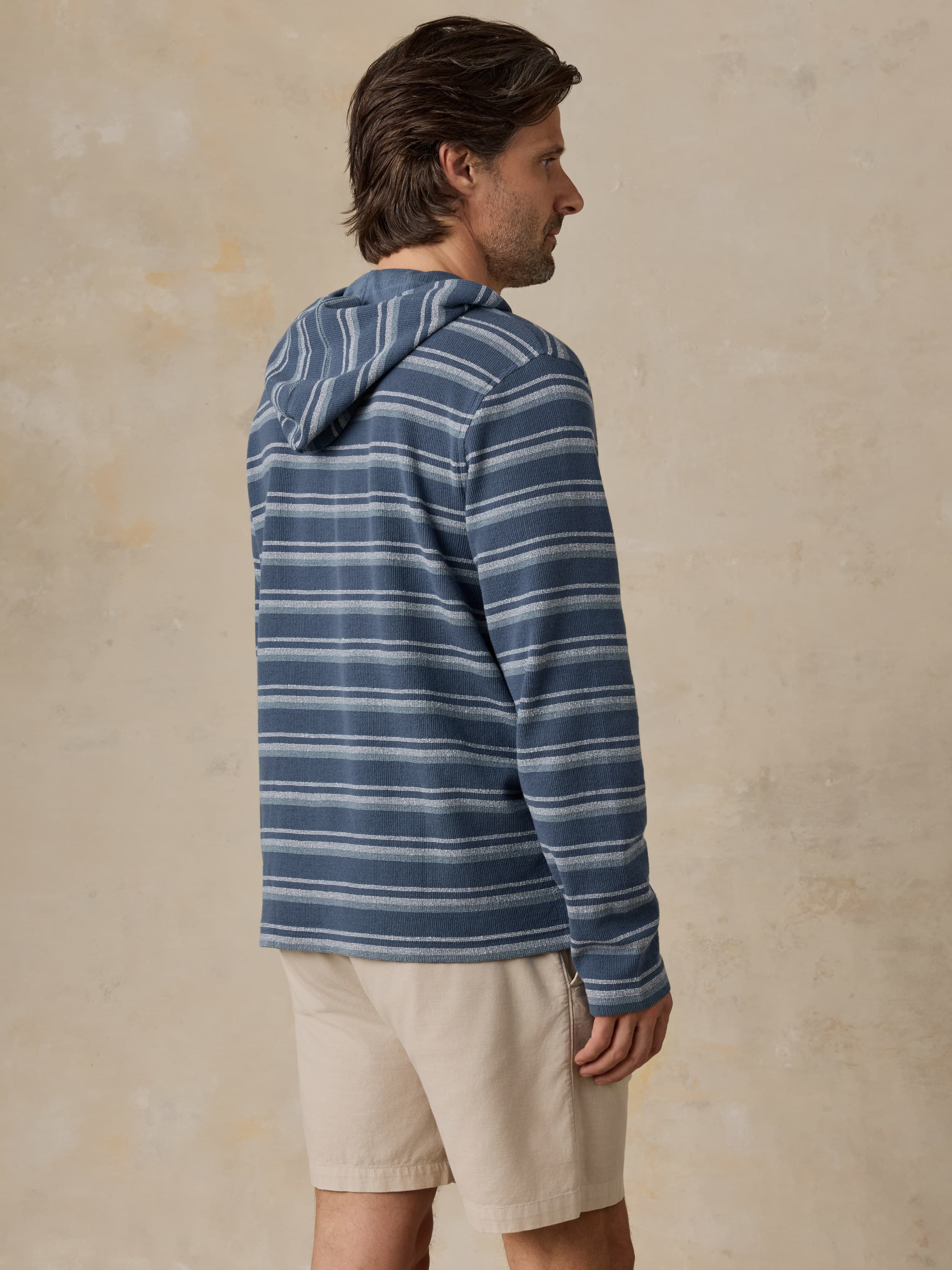 Man wearing a blue striped hoodie with beige shorts against a beige background