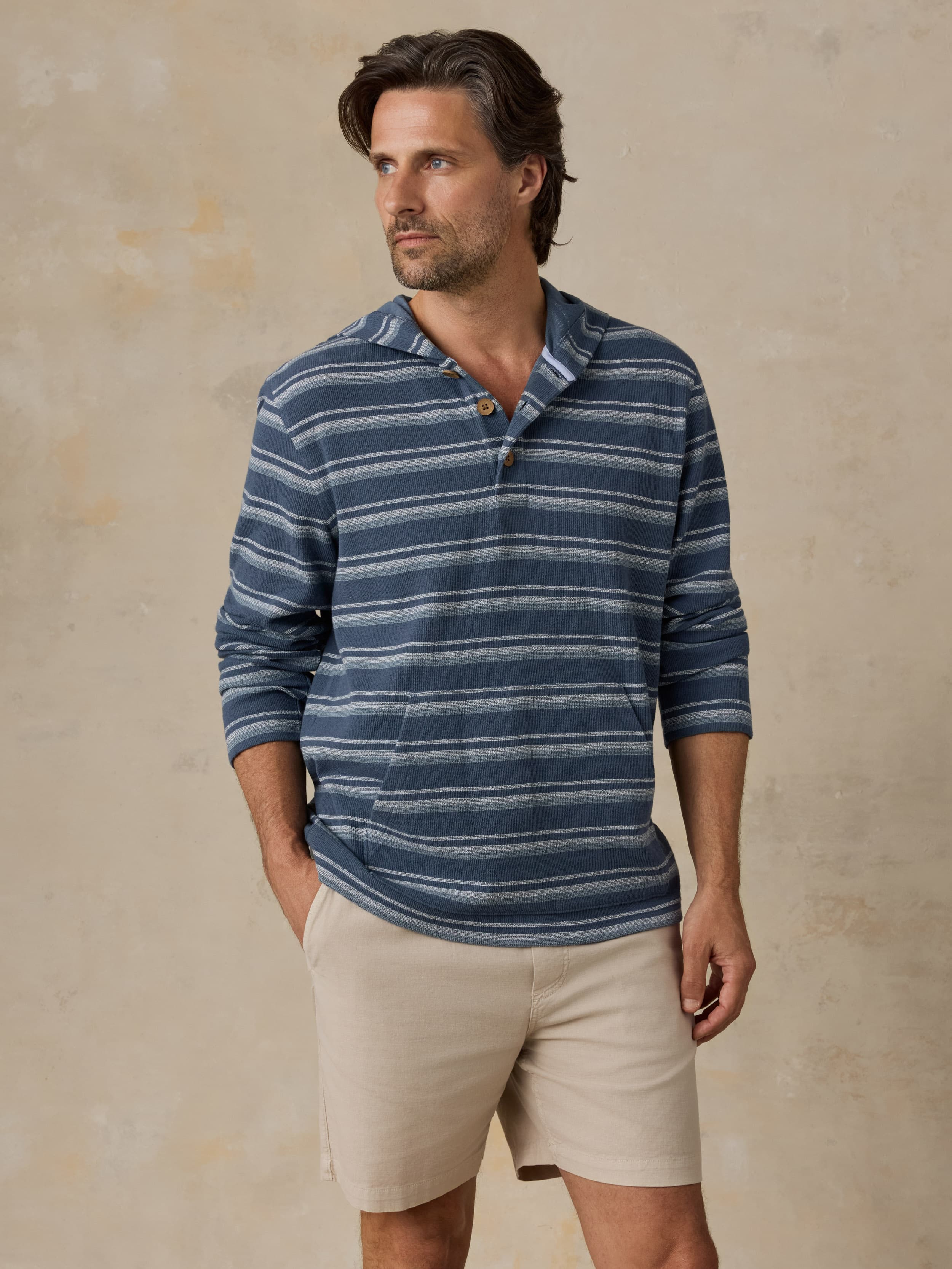 Man wearing a blue striped hoodie and beige shorts against a beige background