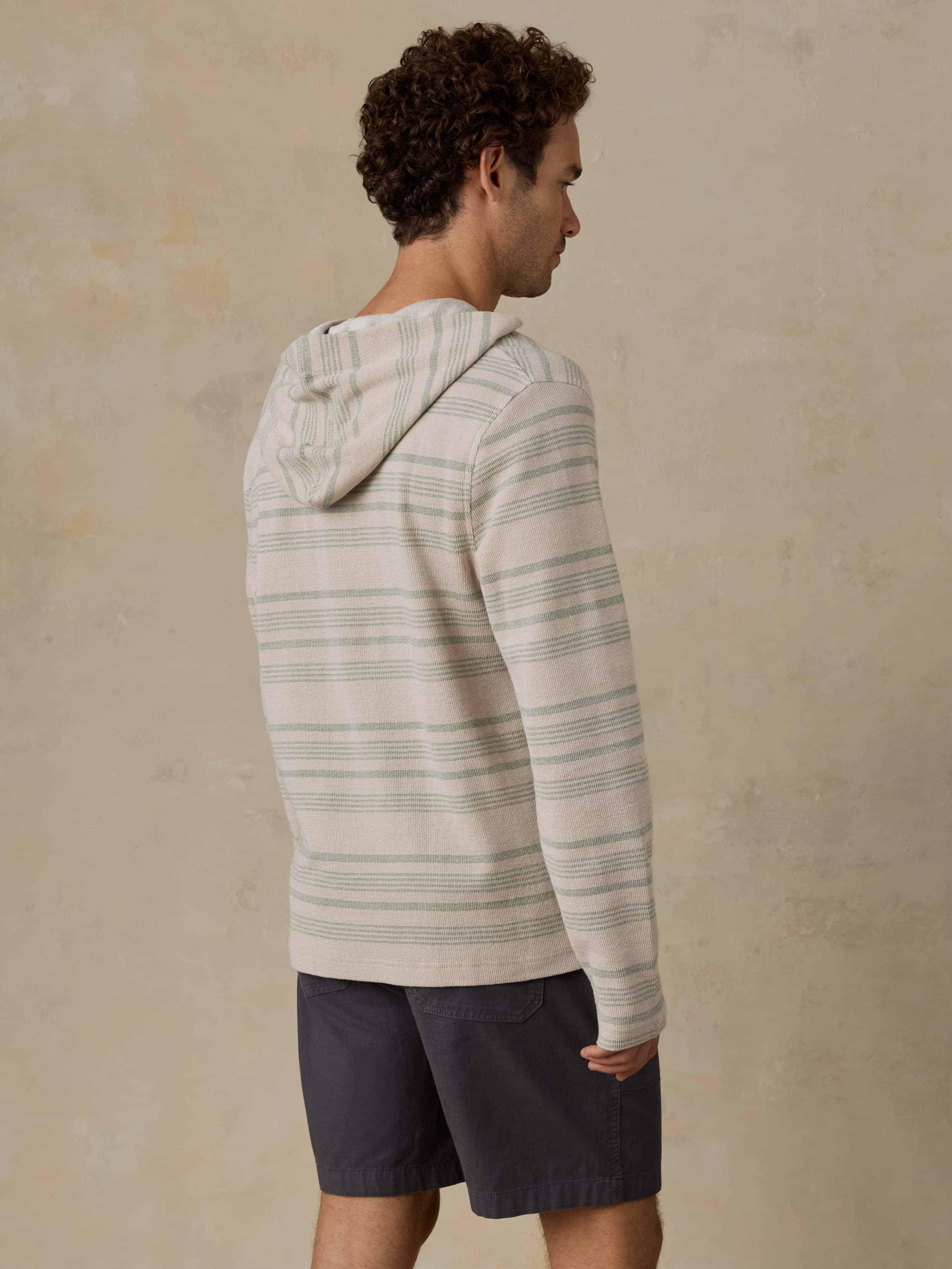 Man wearing a striped hoodie and dark shorts against a beige background