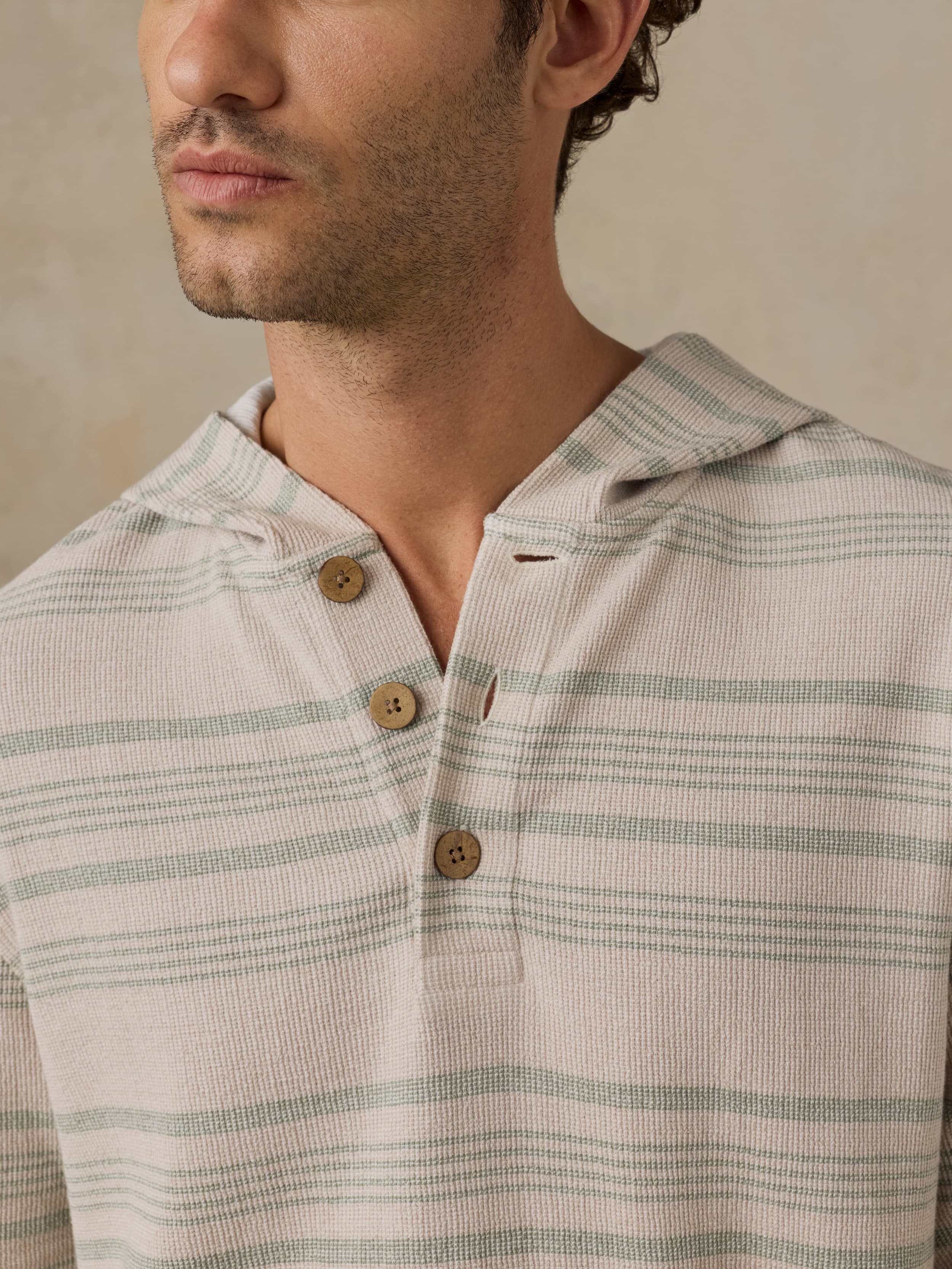 Man wearing a beige and green striped sweatshirt with wooden buttons against a neutral background