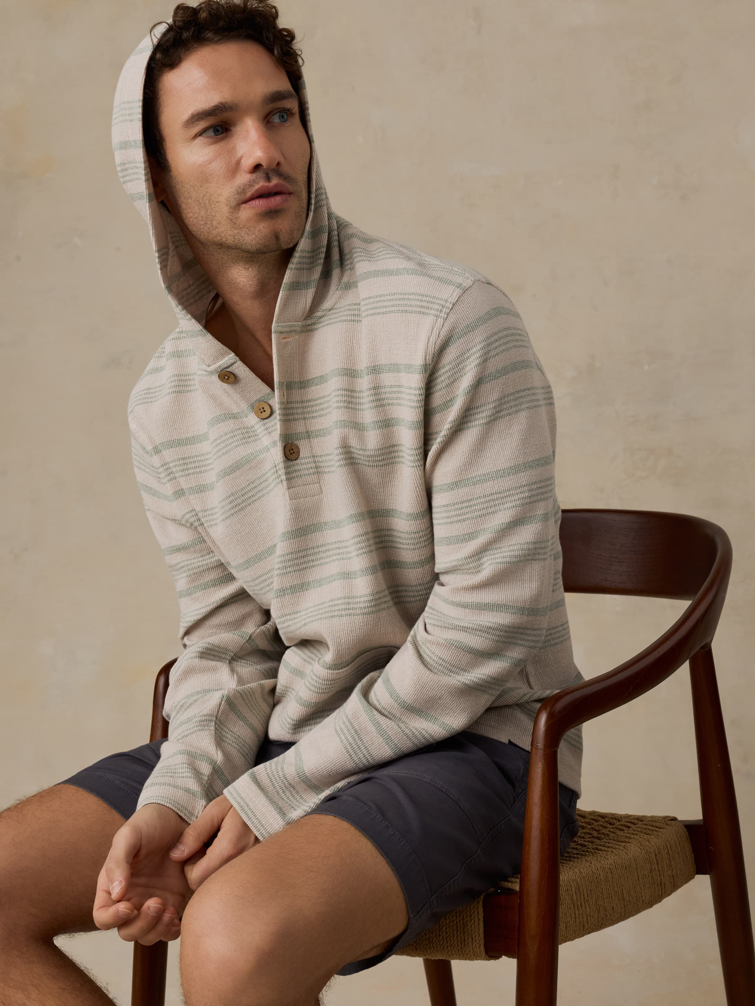 Man wearing a striped hoodie sitting on a chair against a beige background