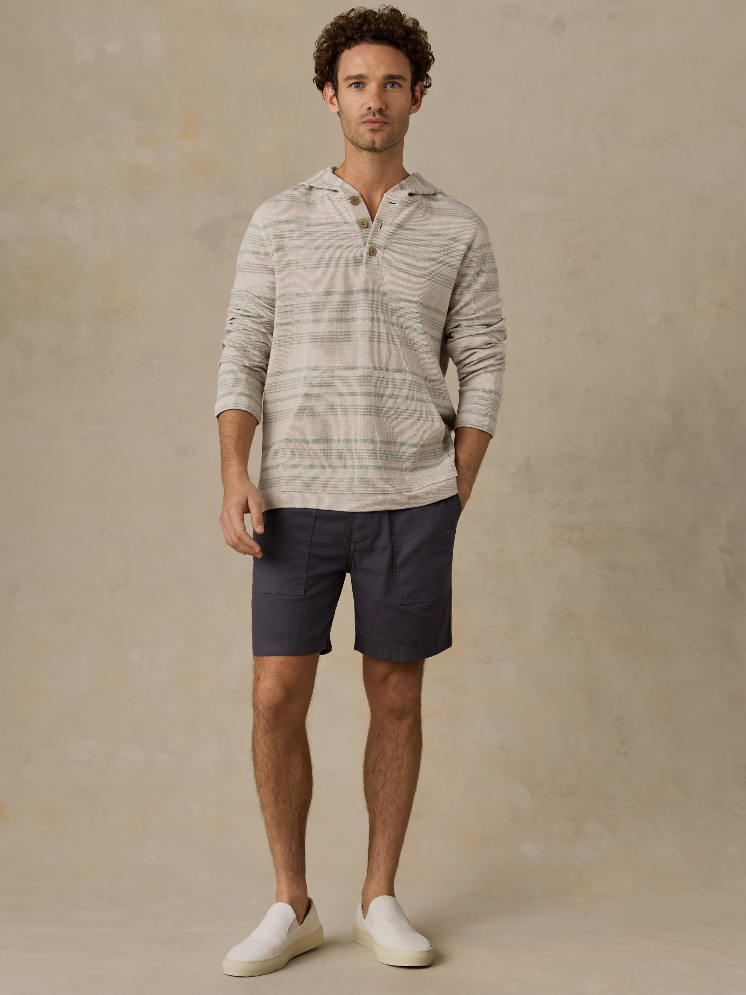 Man wearing a striped sweatshirt and shorts against a beige background