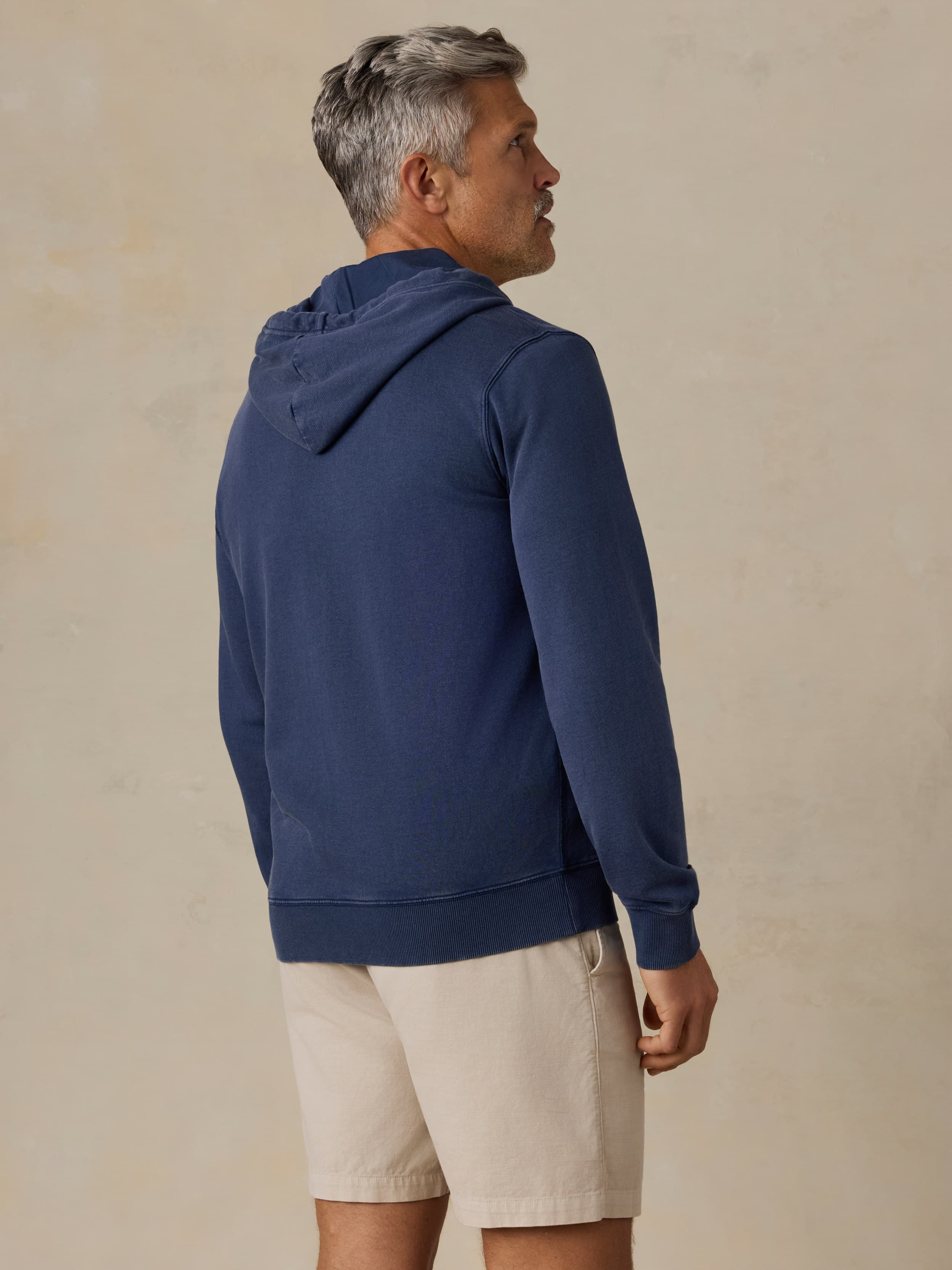 Man wearing a Faherty x Quiksilver blue hoodie and beige shorts against a beige background