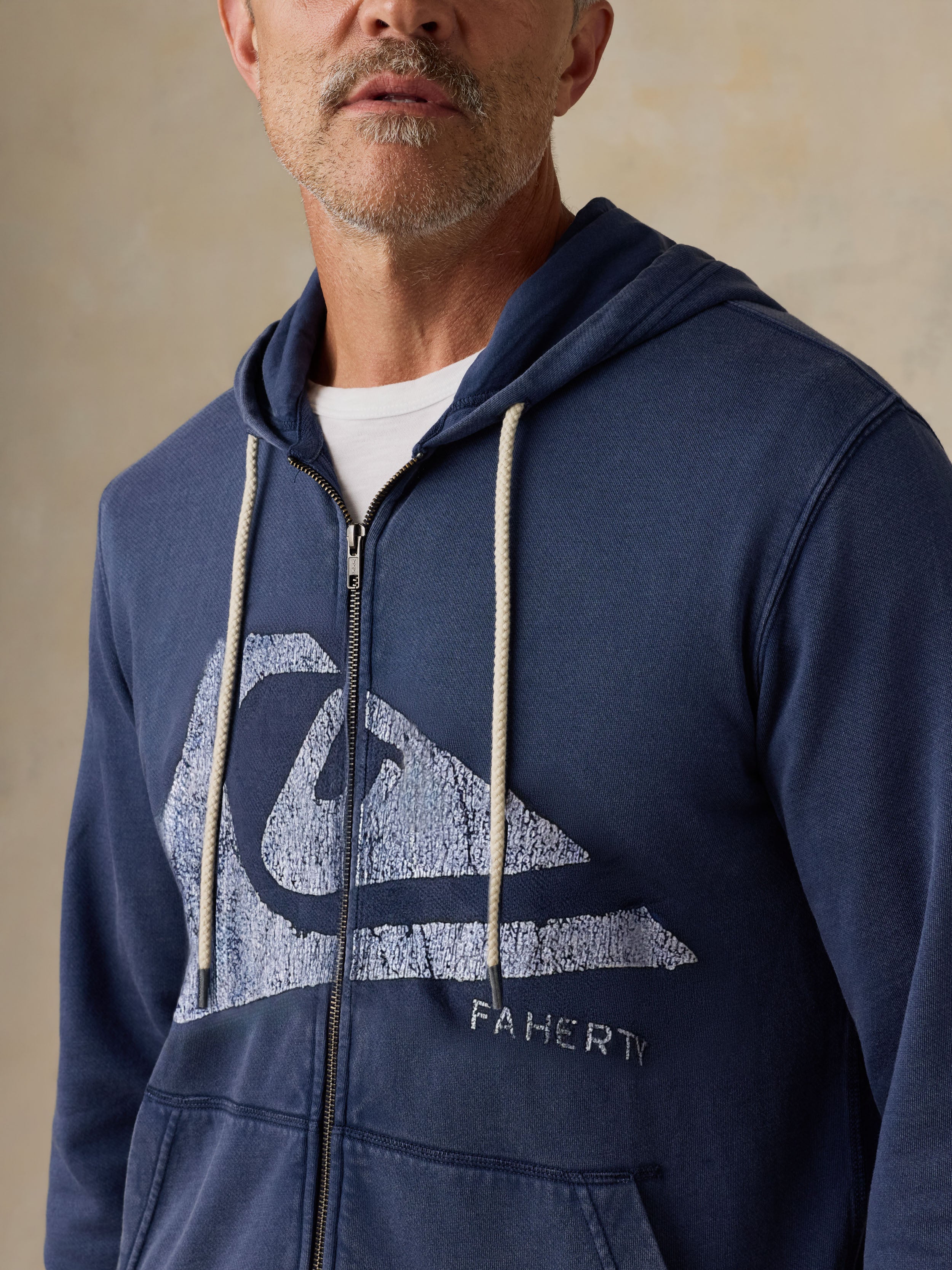 Man wearing a blue hoodie with a Faherty x Quiksilver logo on a beige background