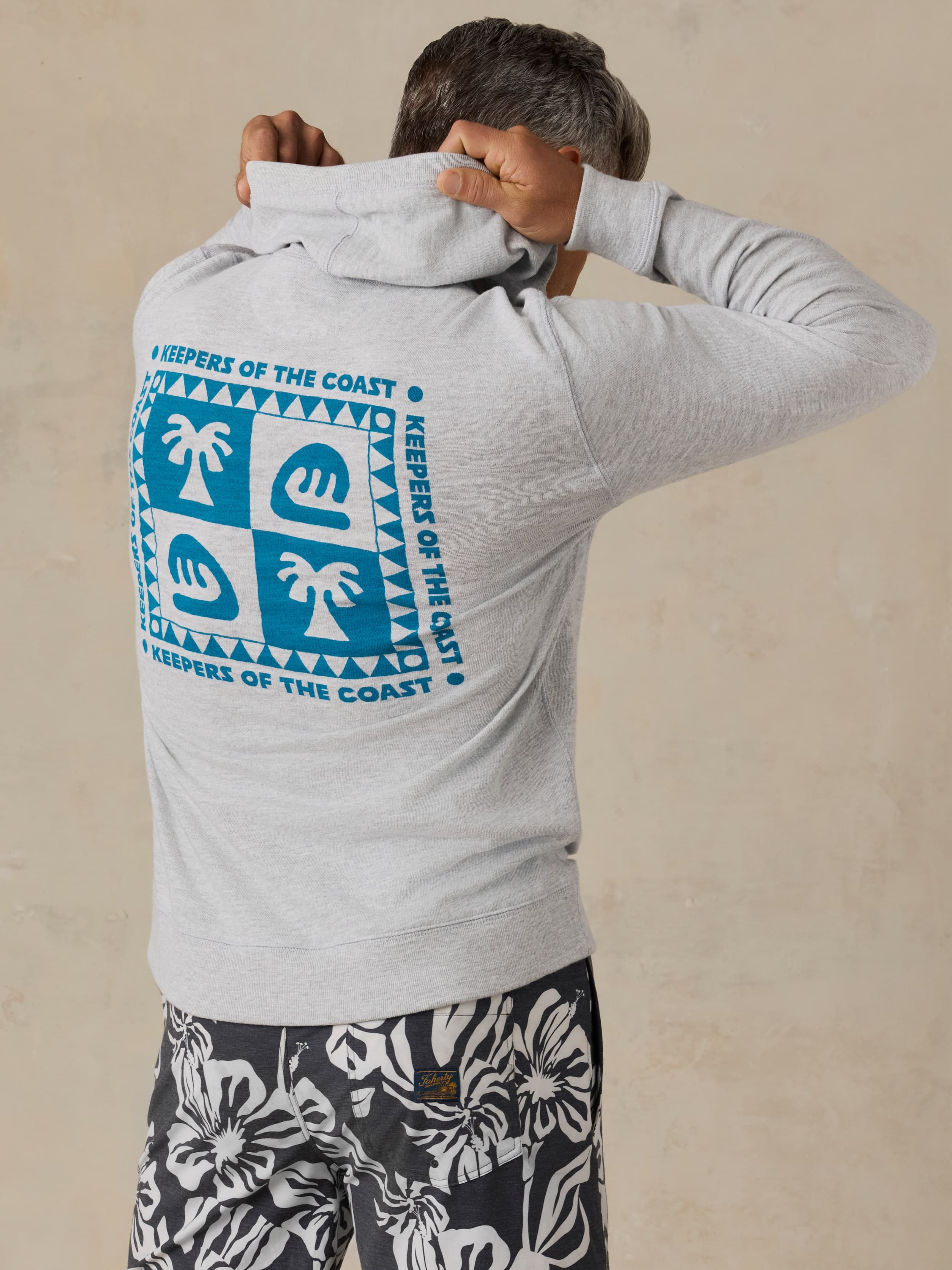 Man wearing a gray hoodie with a Faherty x Surfrider Foundation logo on a beige background