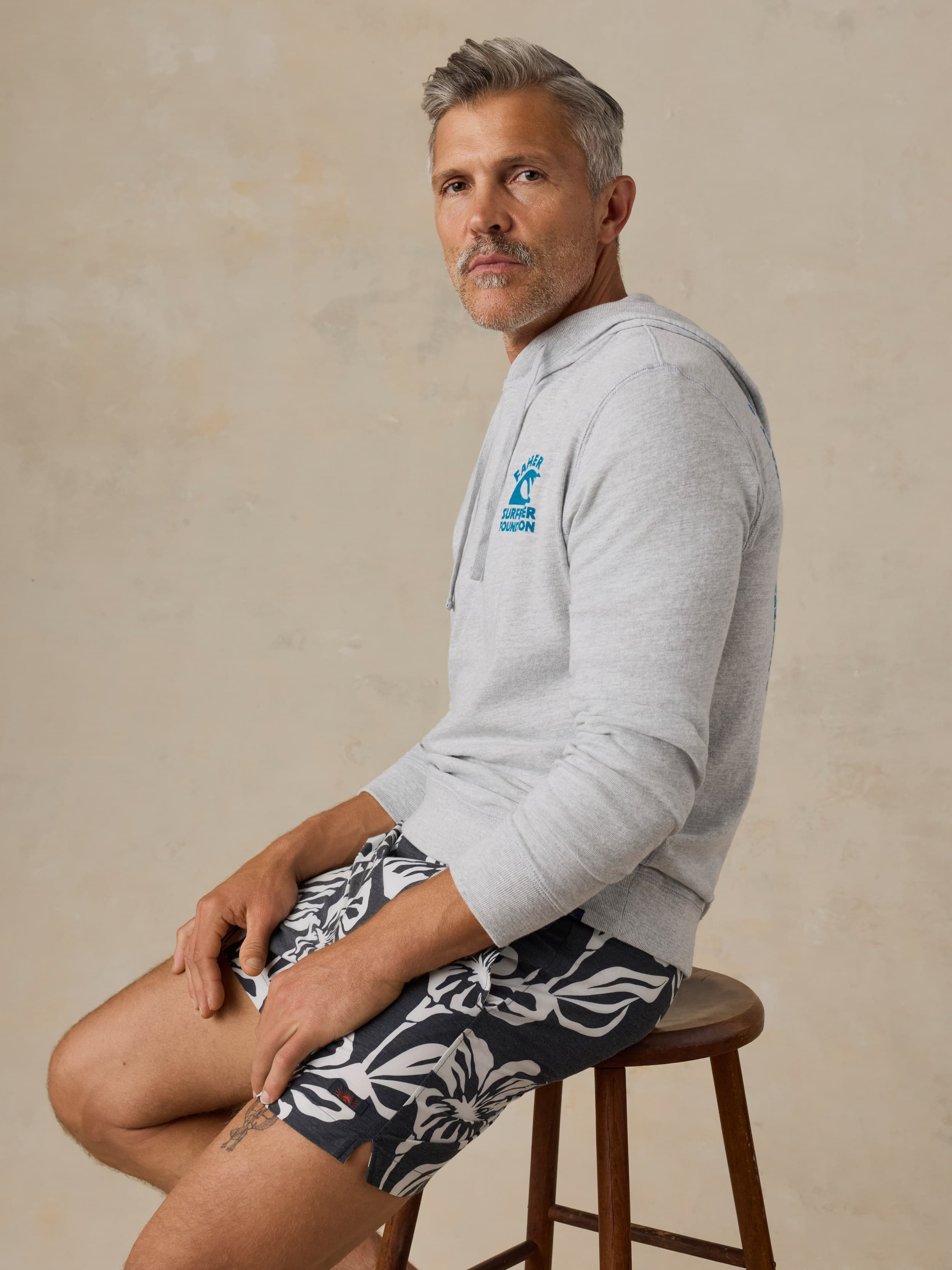 Man wearing a gray hoodie with a Faherty x Surfrider Foundation logo on a beige background