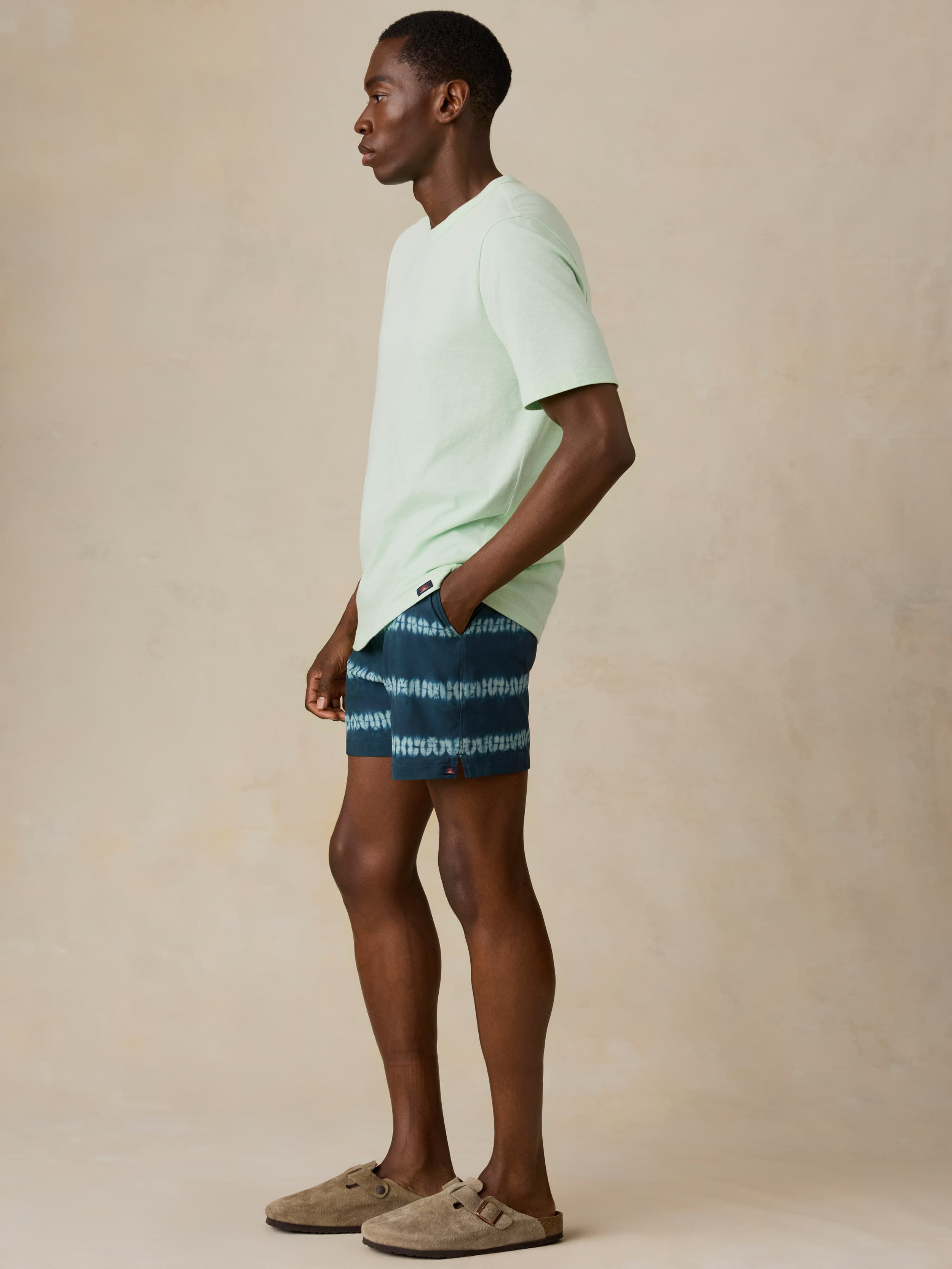 Man wearing a light green t-shirt and blue tie dye swim trunks on a beige background