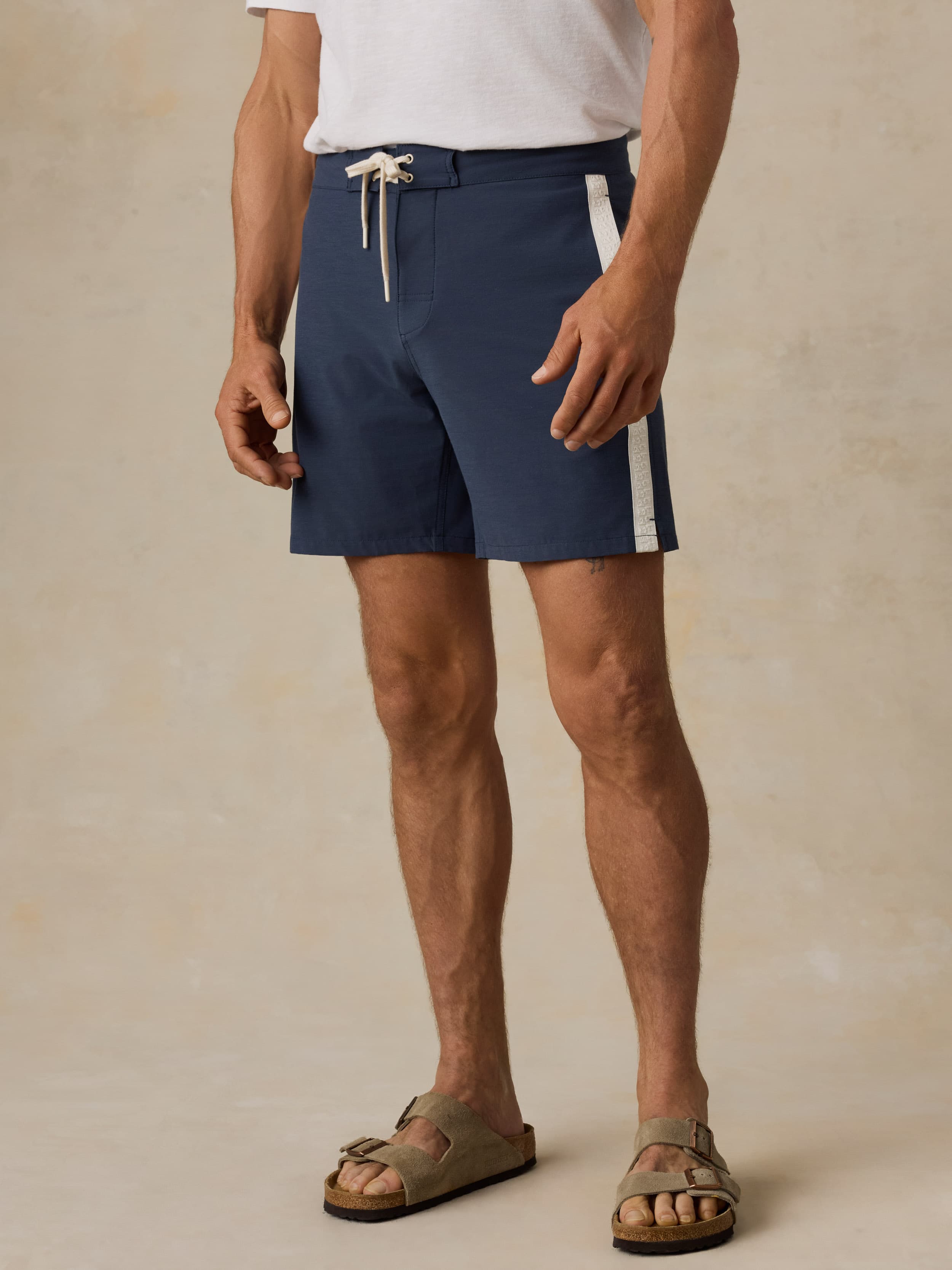 Man wearing navy swim shorts with a white stripe on a beige background