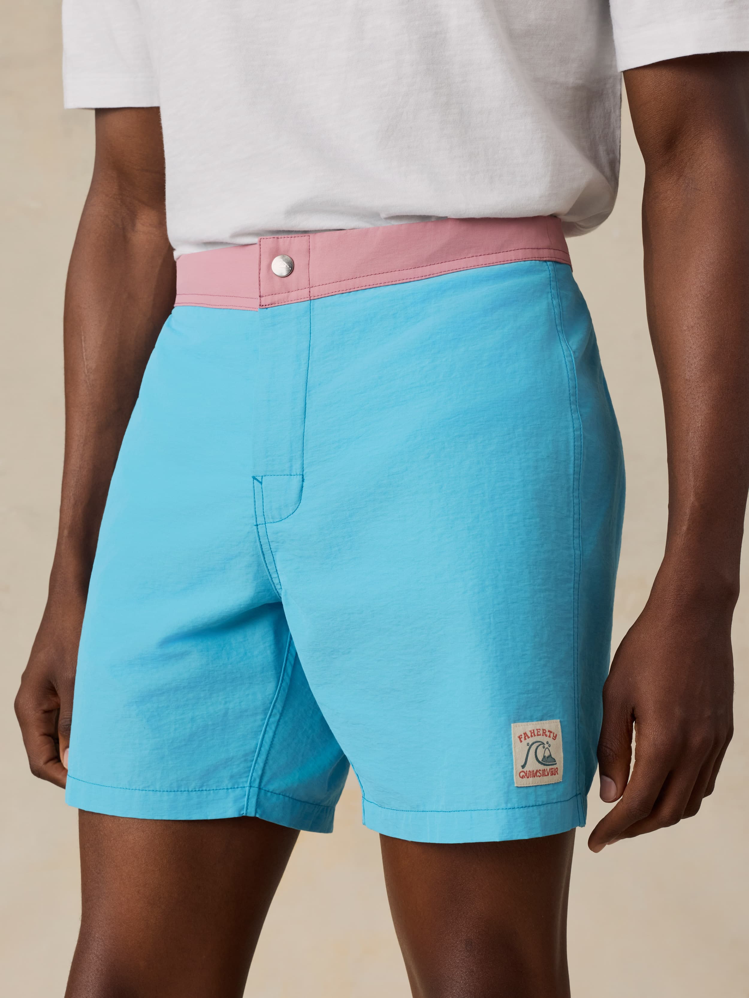 Man wearing blue swim shorts with a pink waistband on a beige background
