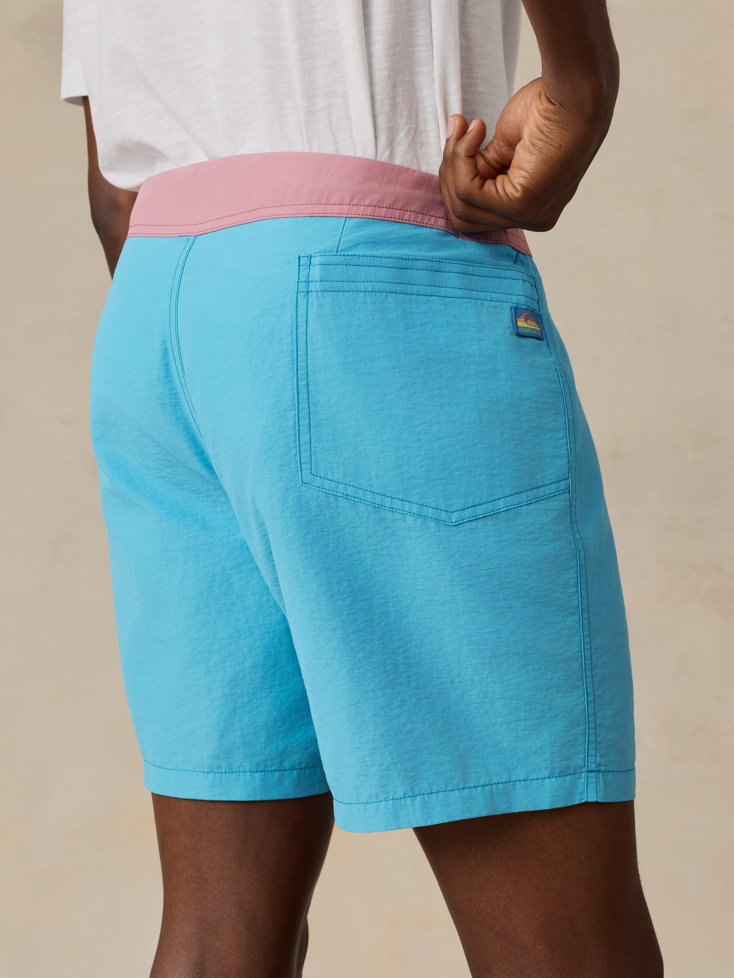 Man wearing blue swim shorts with a pink waistband on a beige background