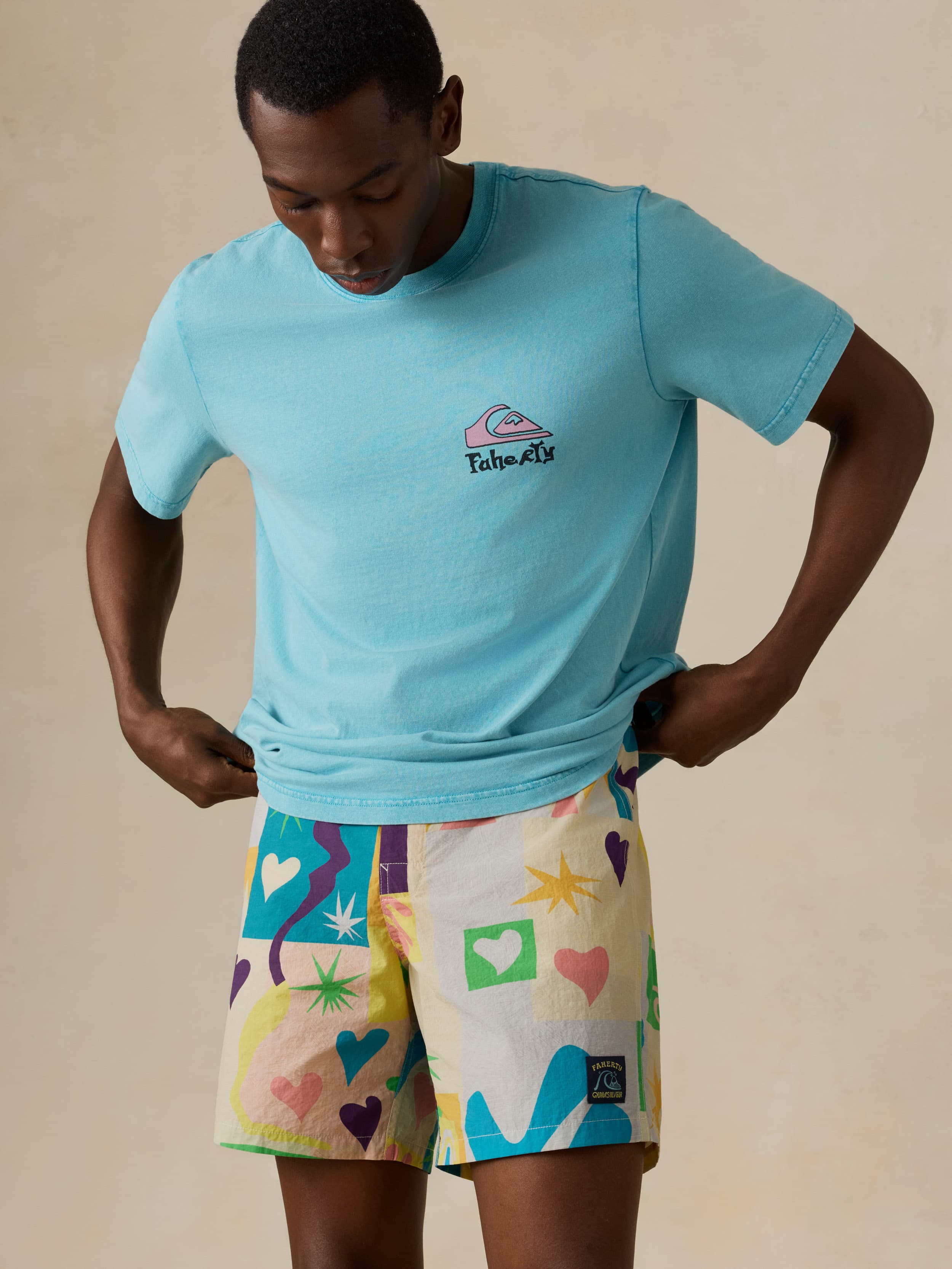 Man wearing a light blue t-shirt and colorful shorts against a beige background