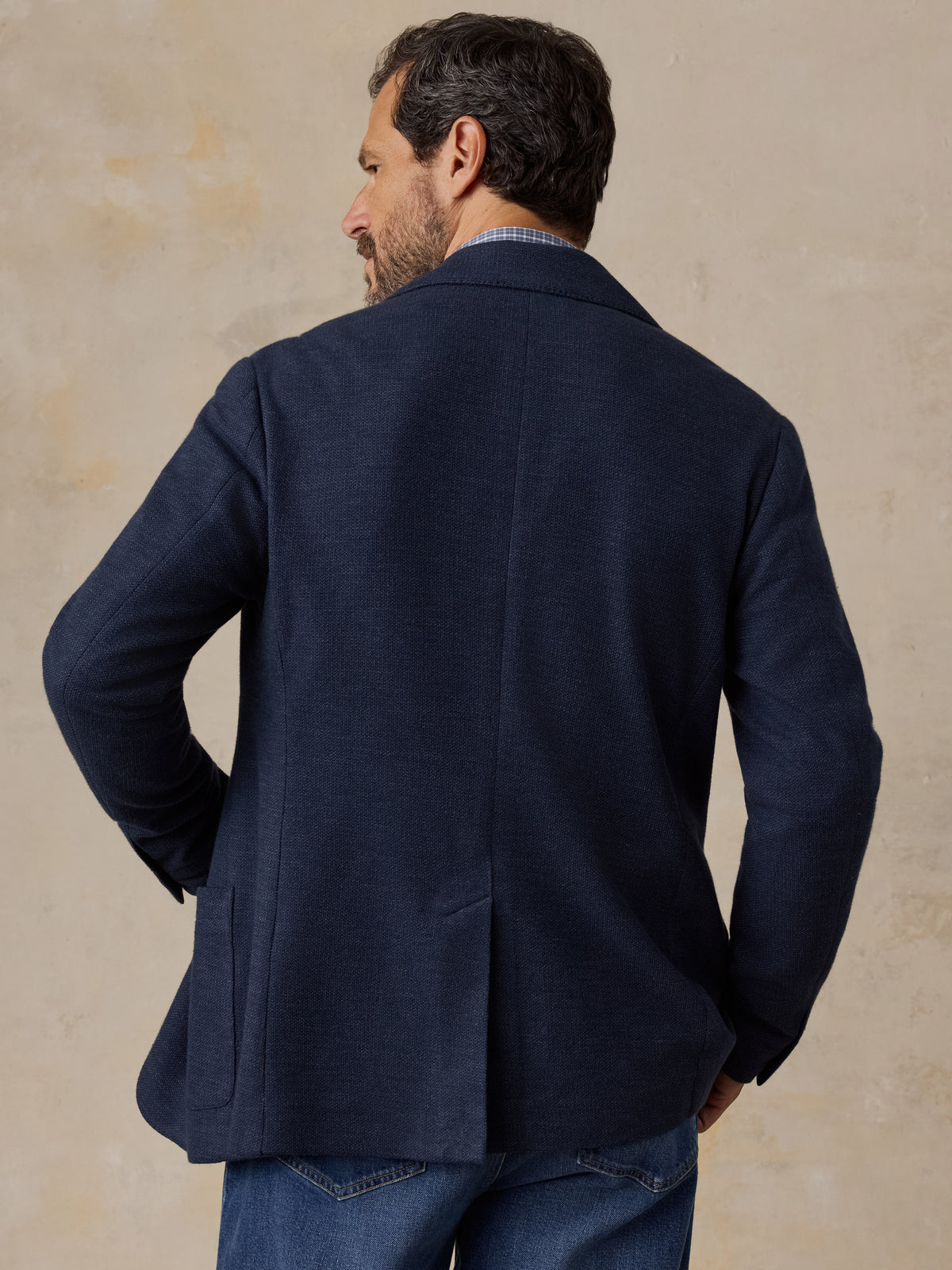 Man wearing a navy blazer over a blue button up shirt and blue jeans, image 2 of 5