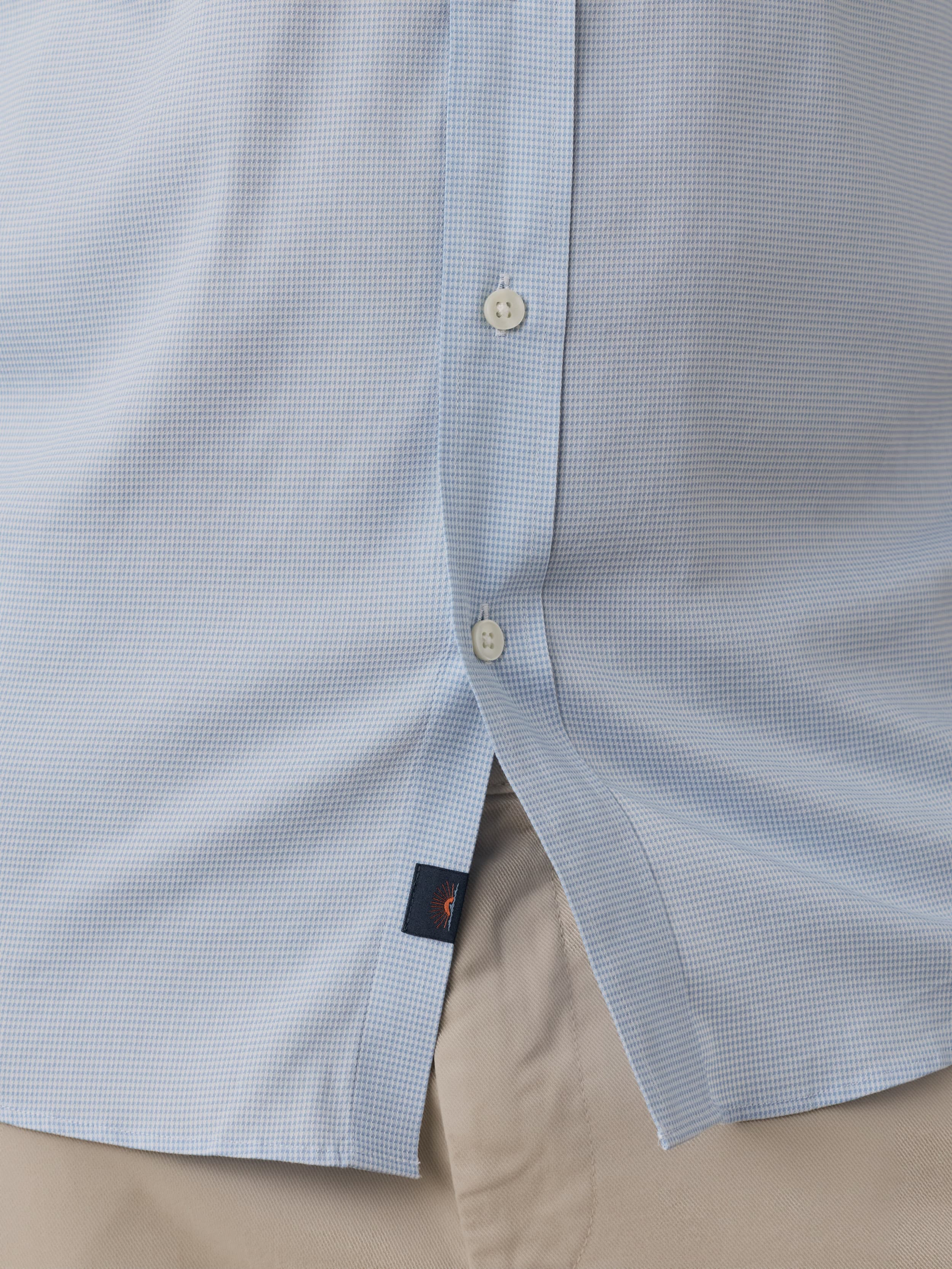 Close-up of a light blue textured shirt with a button and Faherty brand label on a beige background