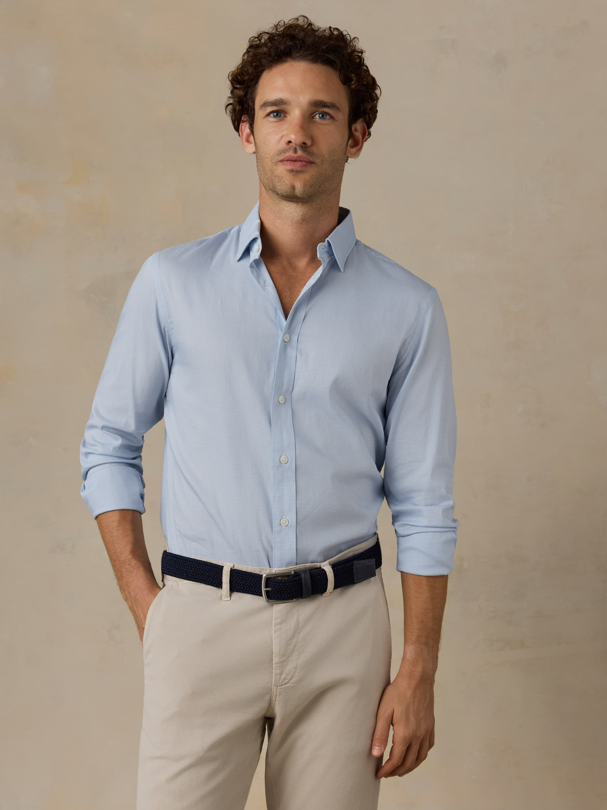 Man wearing a light blue dress shirt and beige pants against a beige background