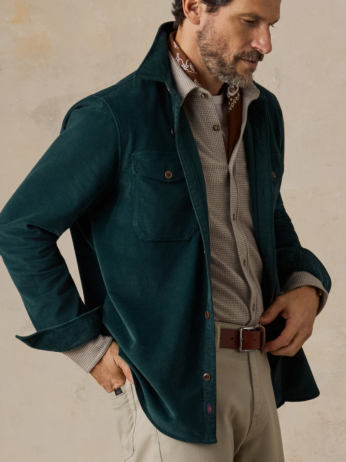 A man wearing a green overshirt, a beige check shirt, and beige pants, image 4 of 5