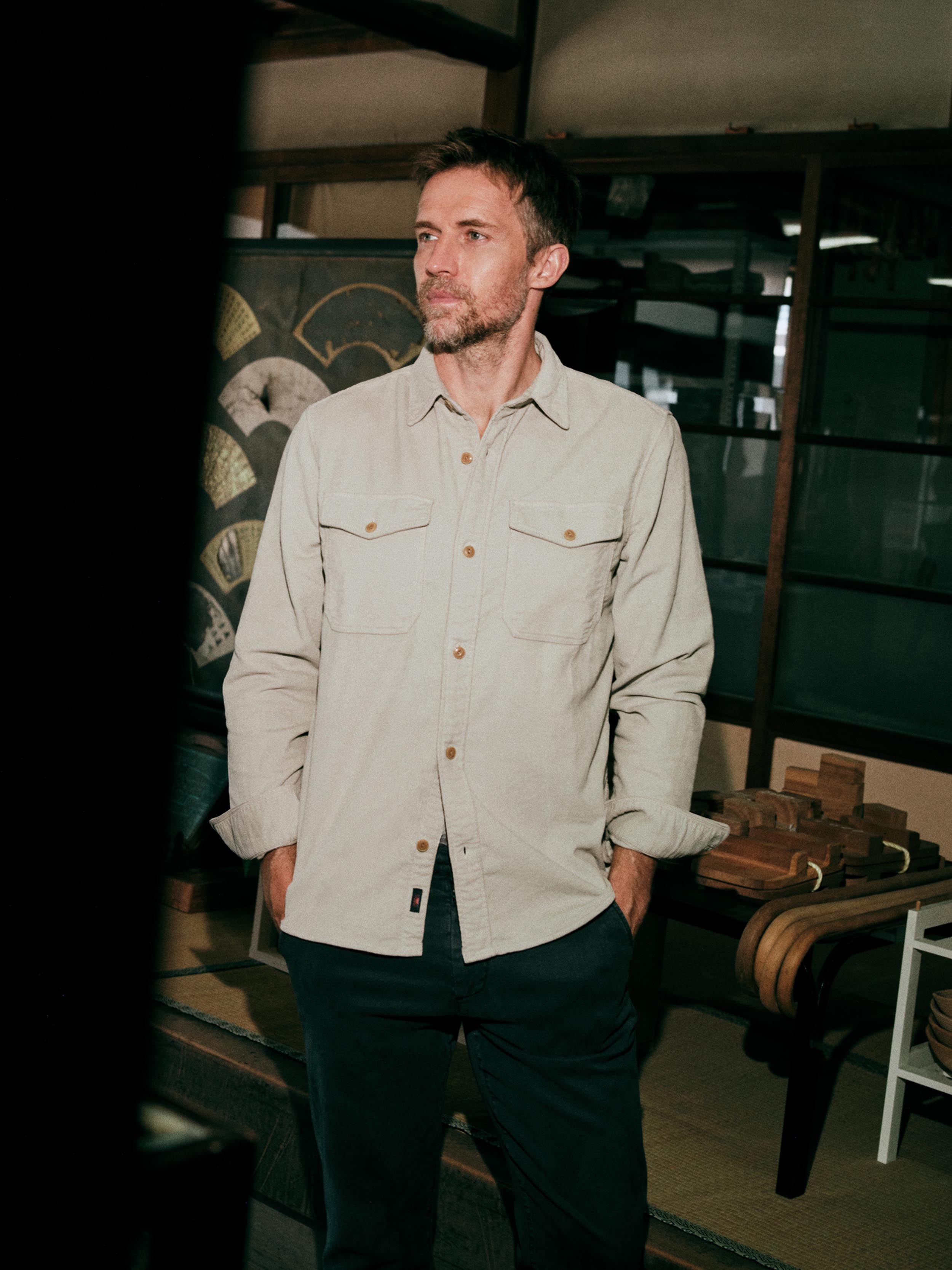 A man wearing a light beige button-down shirt with brown buttons and dark pants