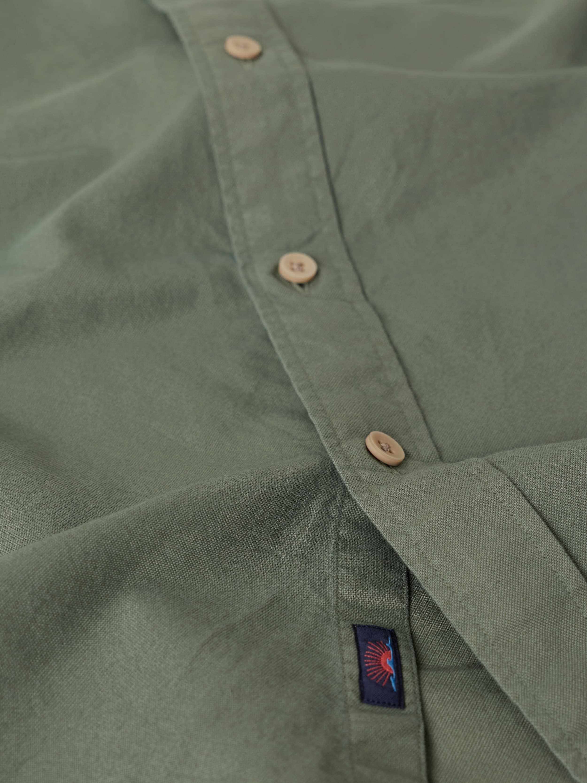Close-up of an olive green button down shirt with a Faherty brand logo on the placket