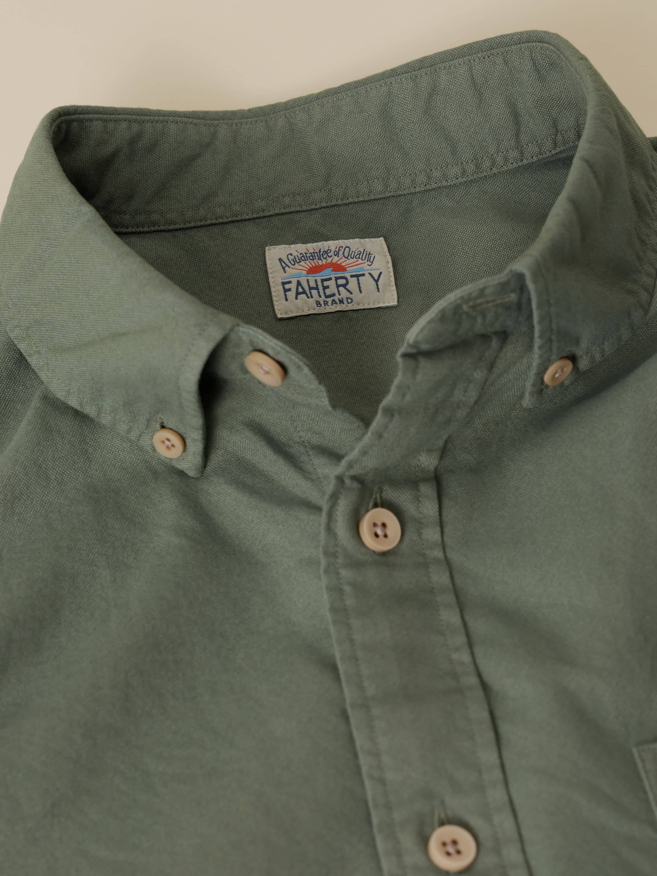 Close-up of an olive green button down shirt with a Faherty brand logo at the neckline
