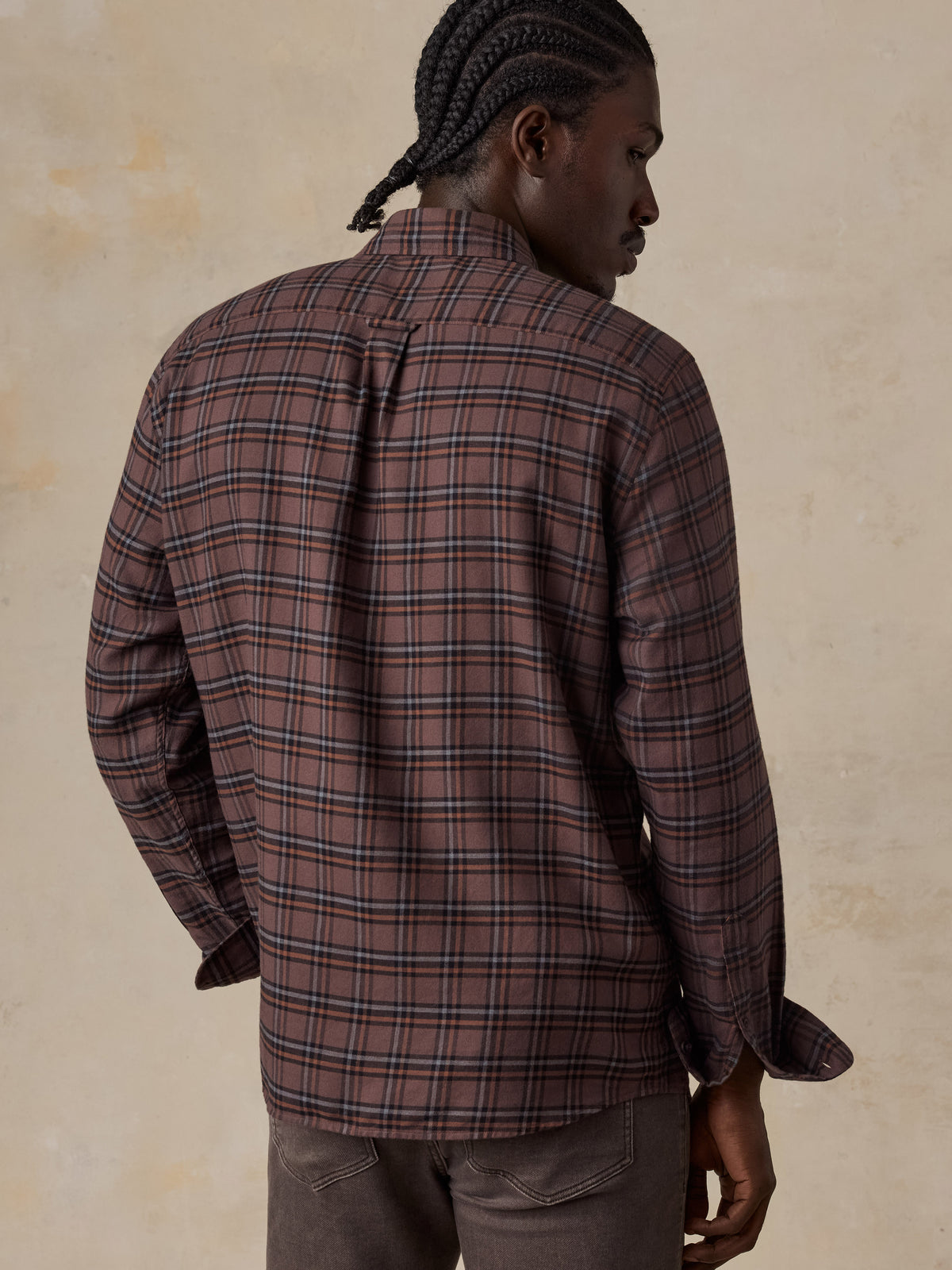 A man viewed from behind wearing a red plaid shirt and brown pants, image 2 of 5